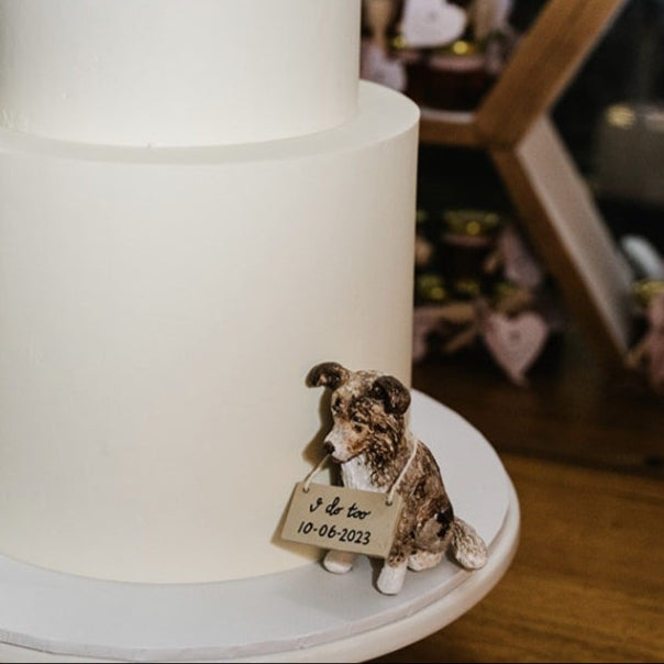 Custom wedding cake topper positioned at the base of a wedding cake with a sign that reads I Do Too.