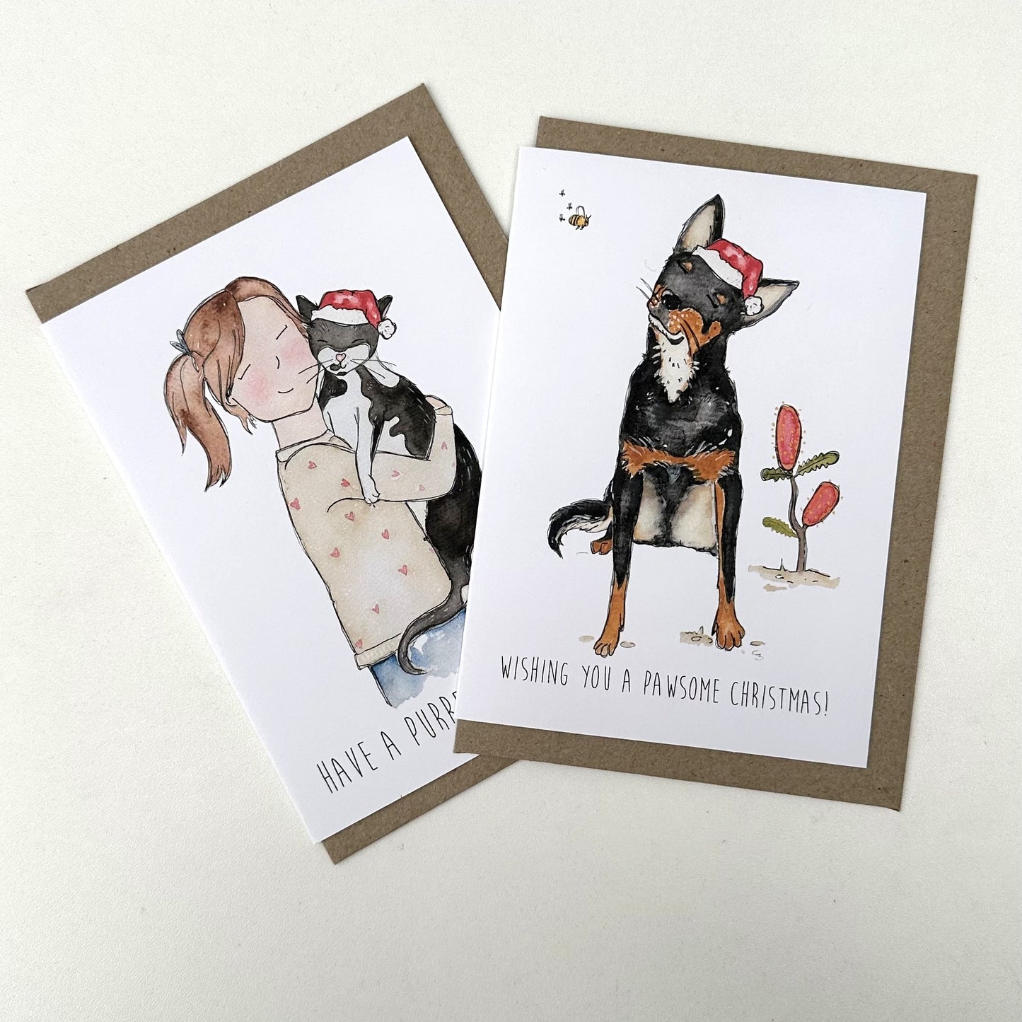 Two Christmas-themed greeting cards featuring illustrations of a girl with a cat and a dog with a Santa hat.