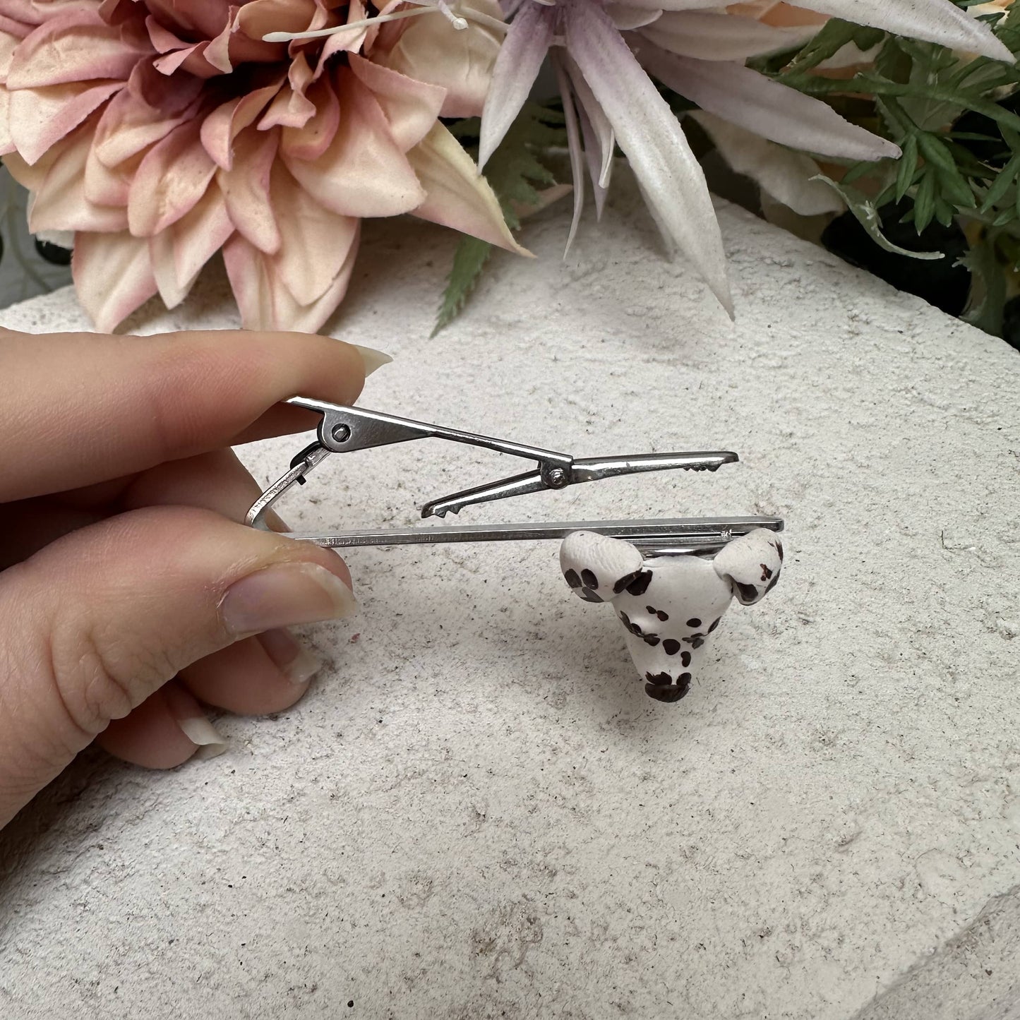 Hand holding a custom dog face tie clip with a small dog design against a floral background