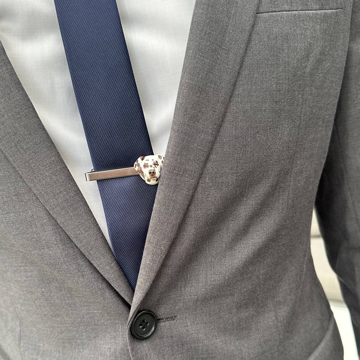 Gray suit jacket with a navy tie and a handmade custom dog face tie clip.