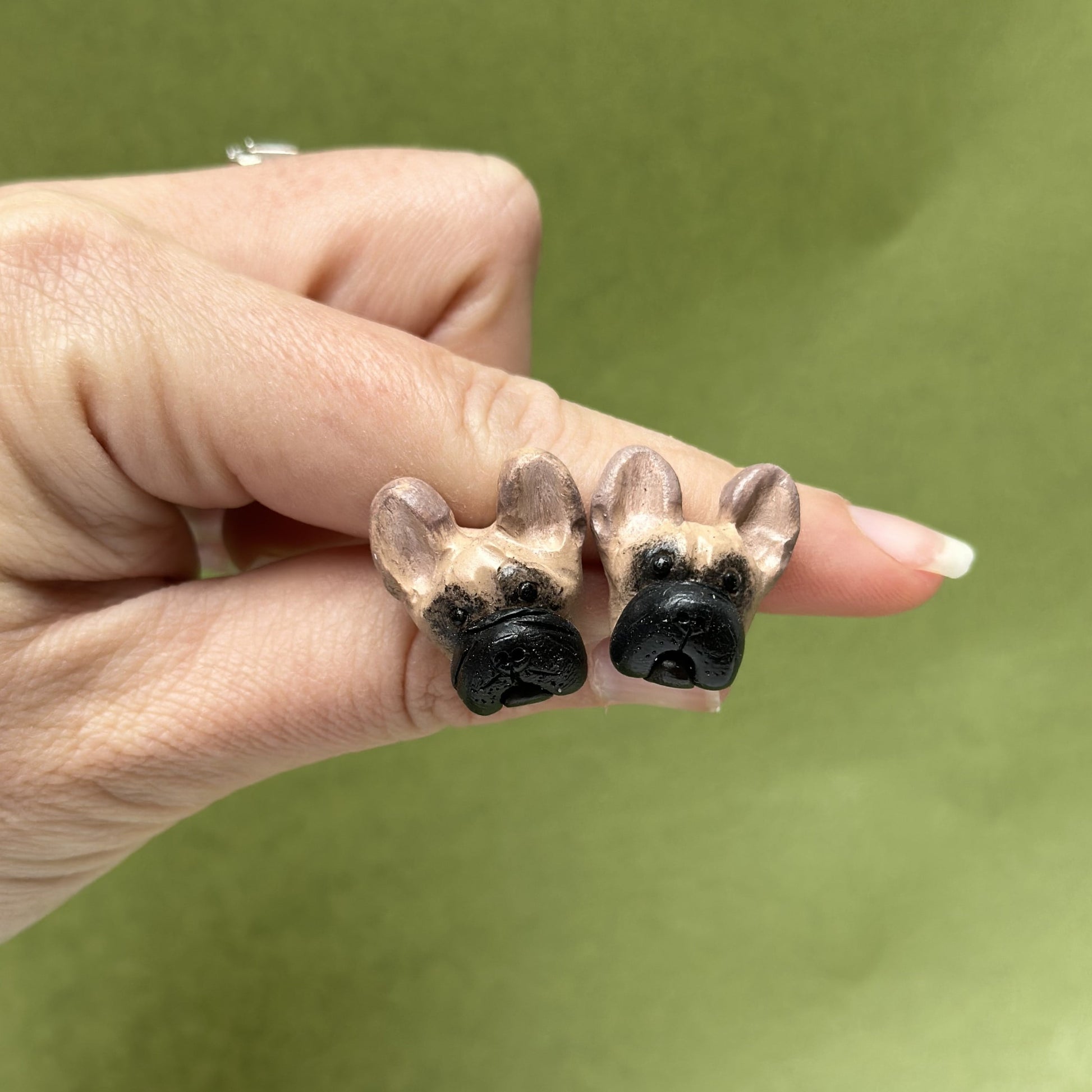 Handmade French bulldog stud earrings by Pawfect Love, positioned in front of green background
