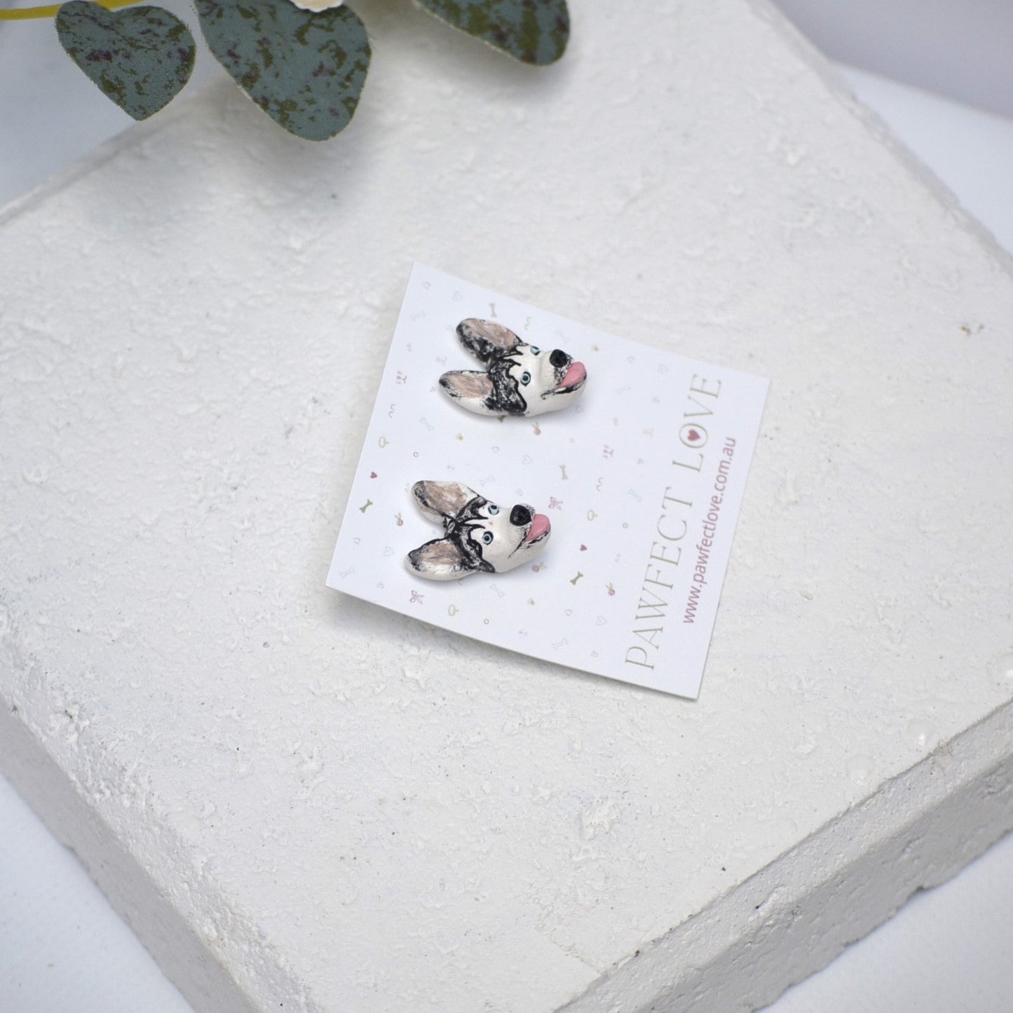 Handmade husky stud earrings by Pawfect Love, positioned in front of white paver