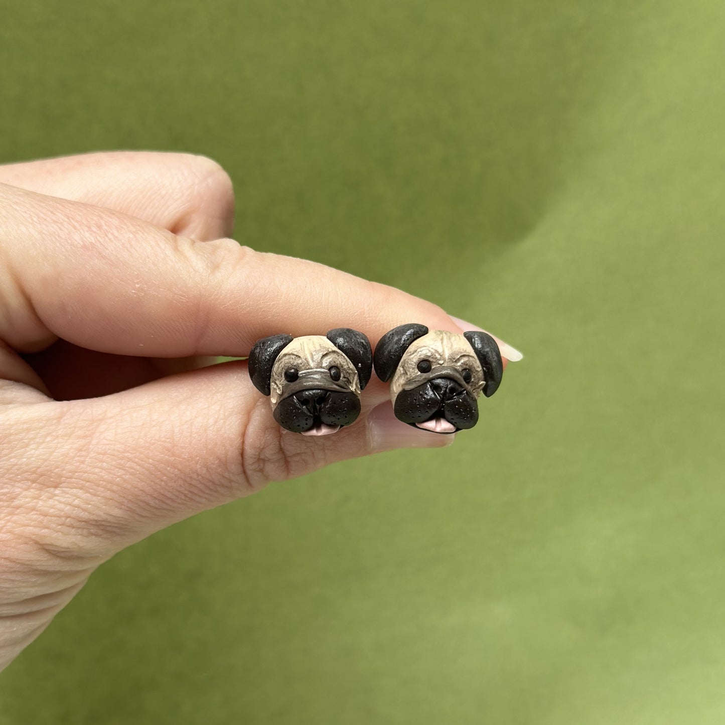 Handmade Pug stud earrings by Pawfect Love, positioned in front of green background