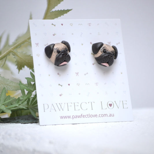 Handmade Pug stud earrings by Pawfect Love, positioned in front of green flower arrangement