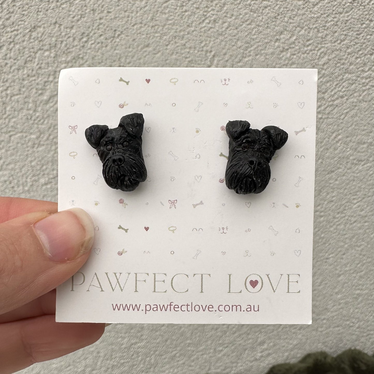 Black schnauzer dog-shaped earrings on a 'Pawfect Love' branded card held by a hand.
