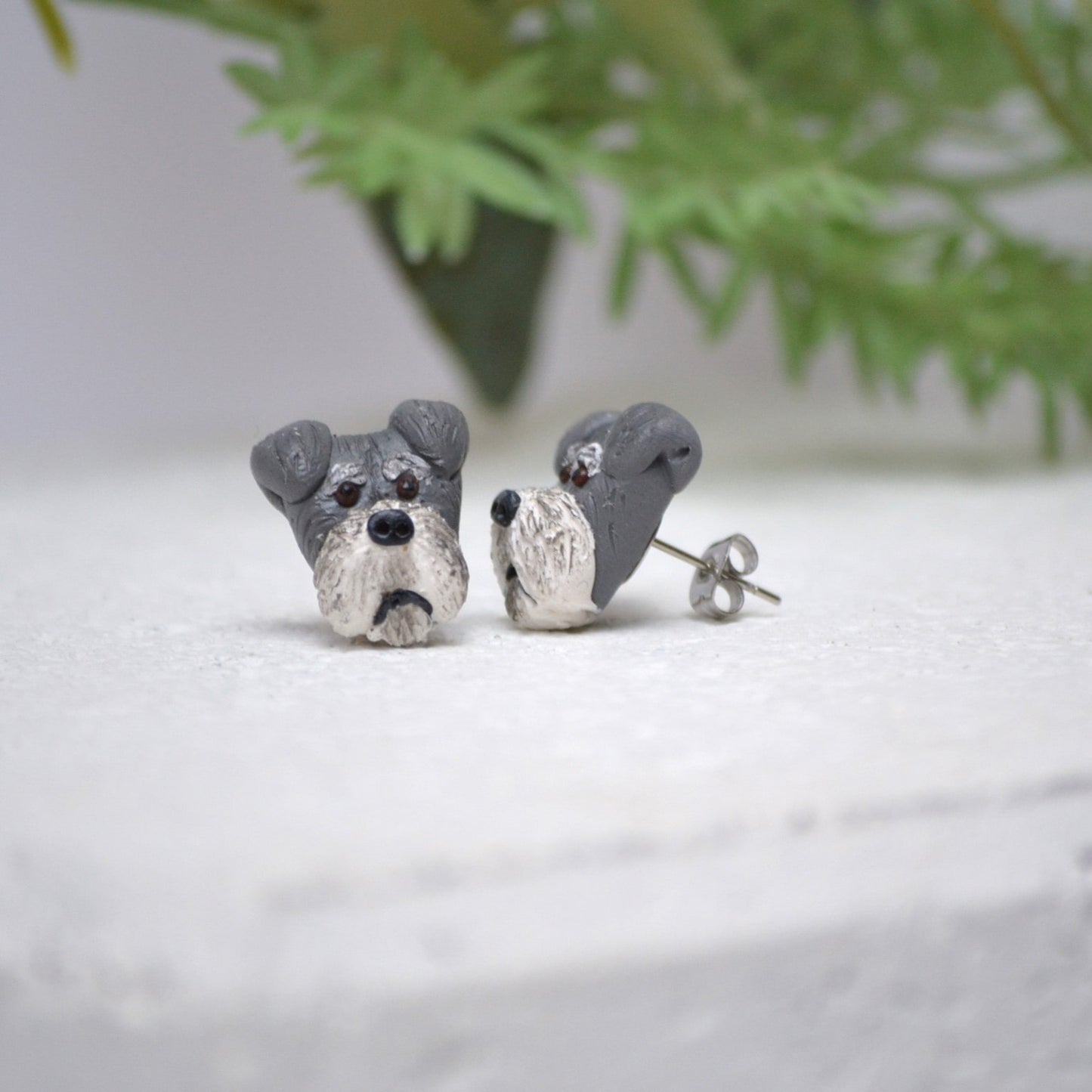 Handmade schnauzer stud earrings by Pawfect Love, positioned in front of green flower arrangement