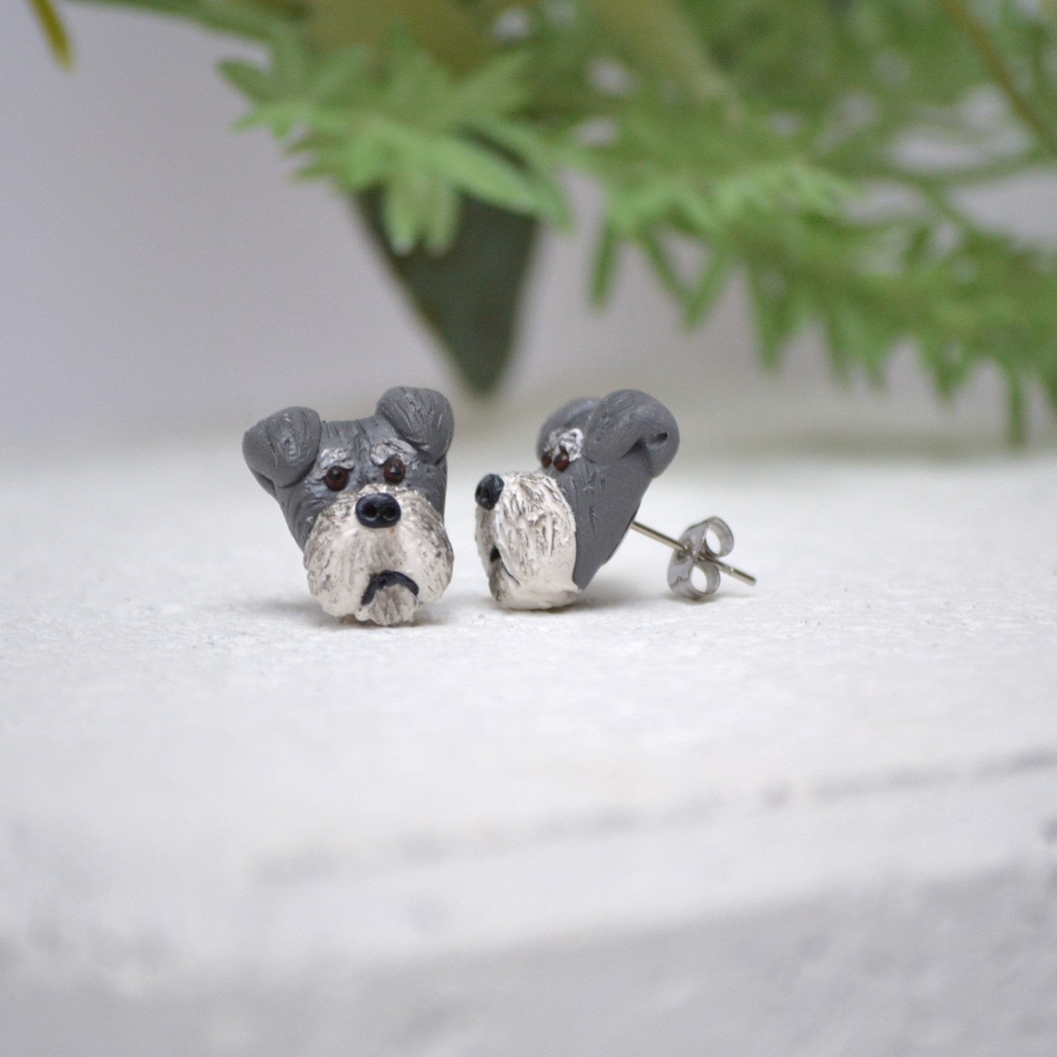 Handmade schnauzer stud earrings by Pawfect Love, positioned in front of green flower arrangement