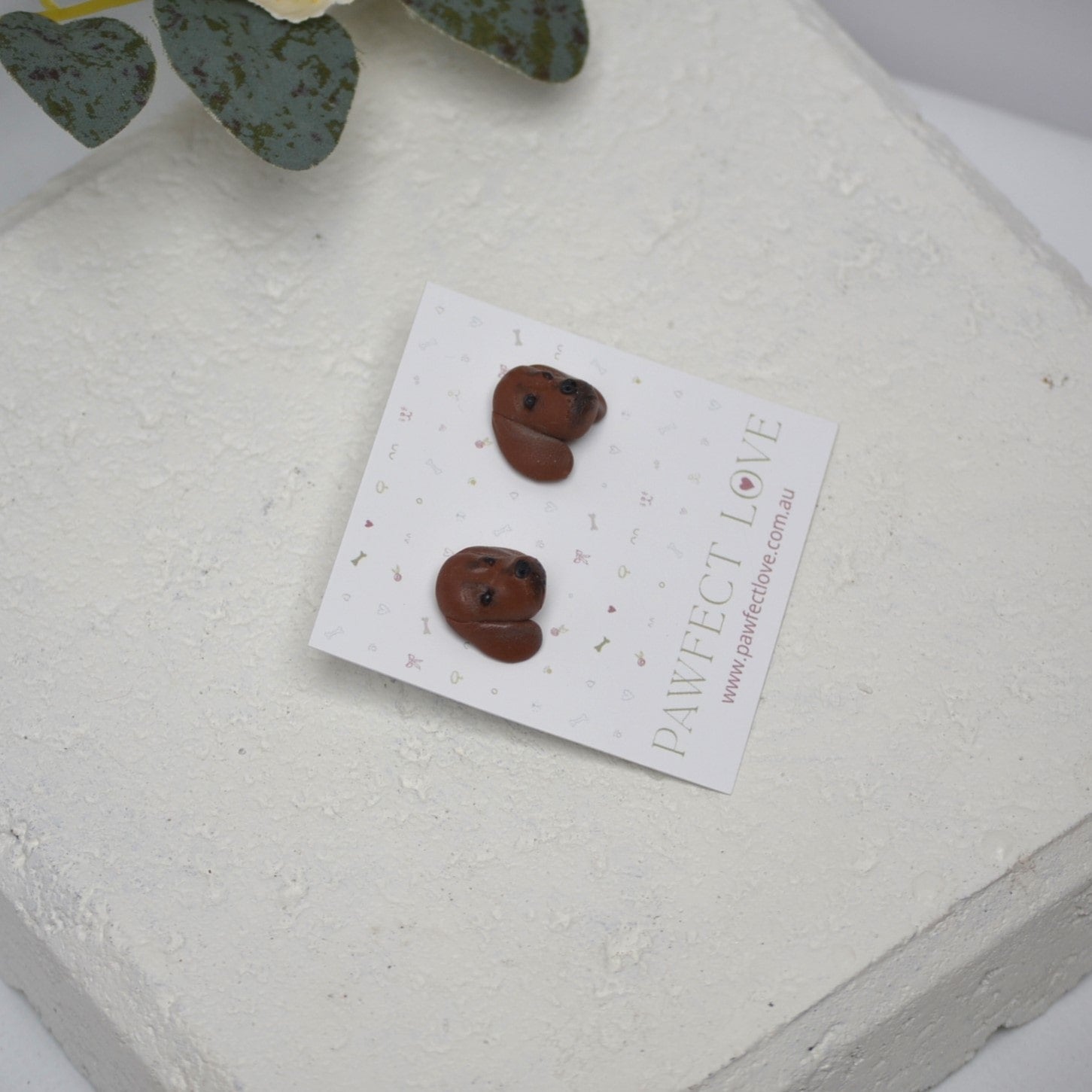 Handmade dachshund stud earrings by Pawfect Love, positioned on white paver