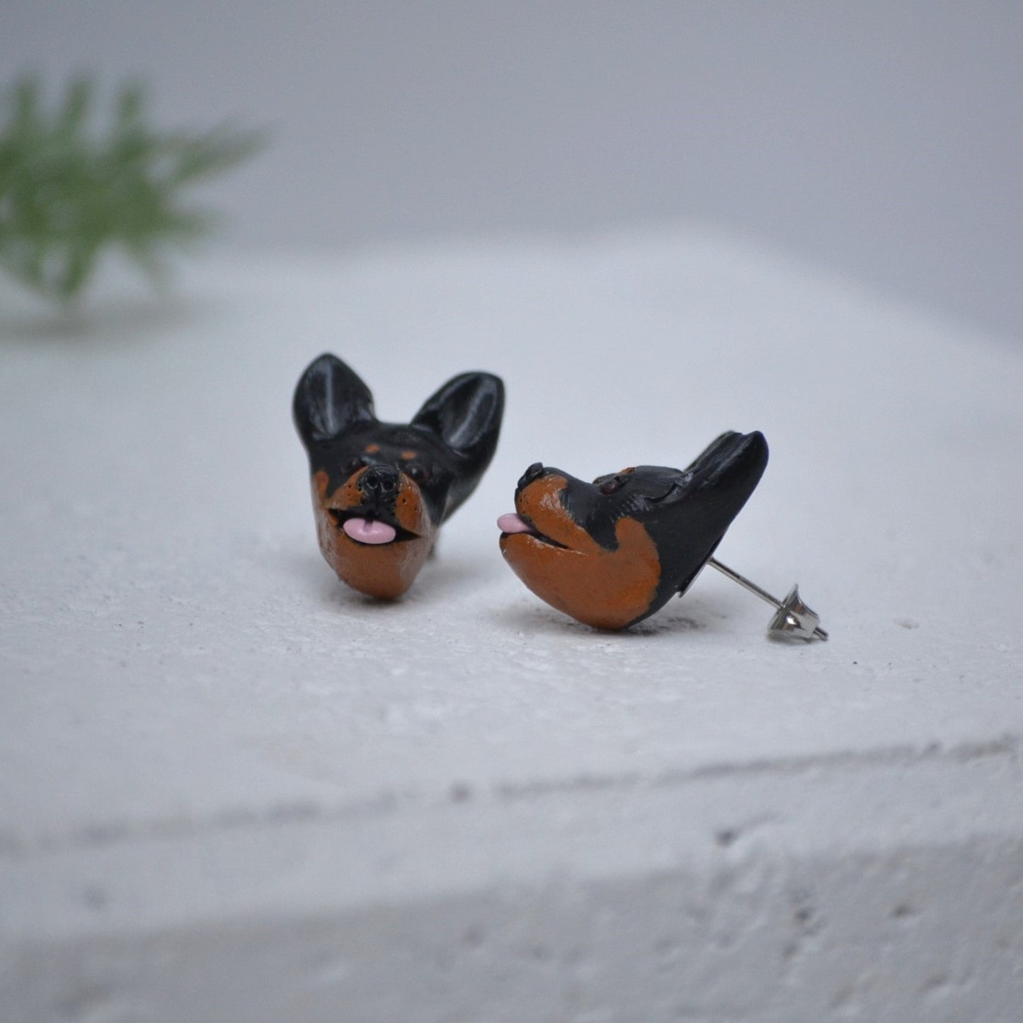 Handmade kelpie stud earrings by Pawfect Love, positioned in front of green flower arrangement