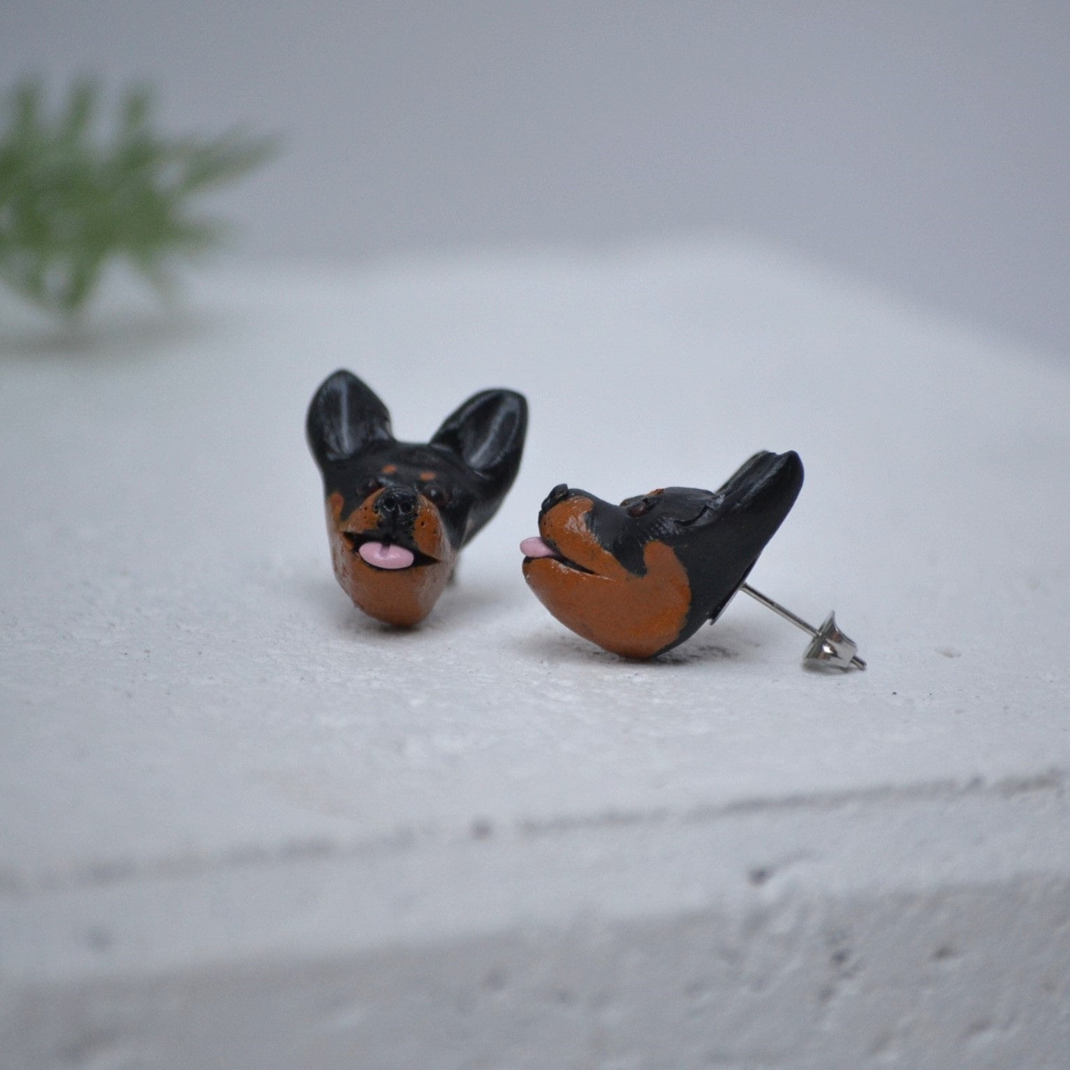 Handmade kelpie stud earrings by Pawfect Love, positioned in front of green flower arrangement
