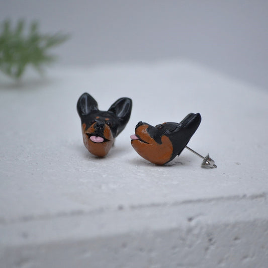 Handmade kelpie stud earrings by Pawfect Love, positioned in front of green flower arrangement