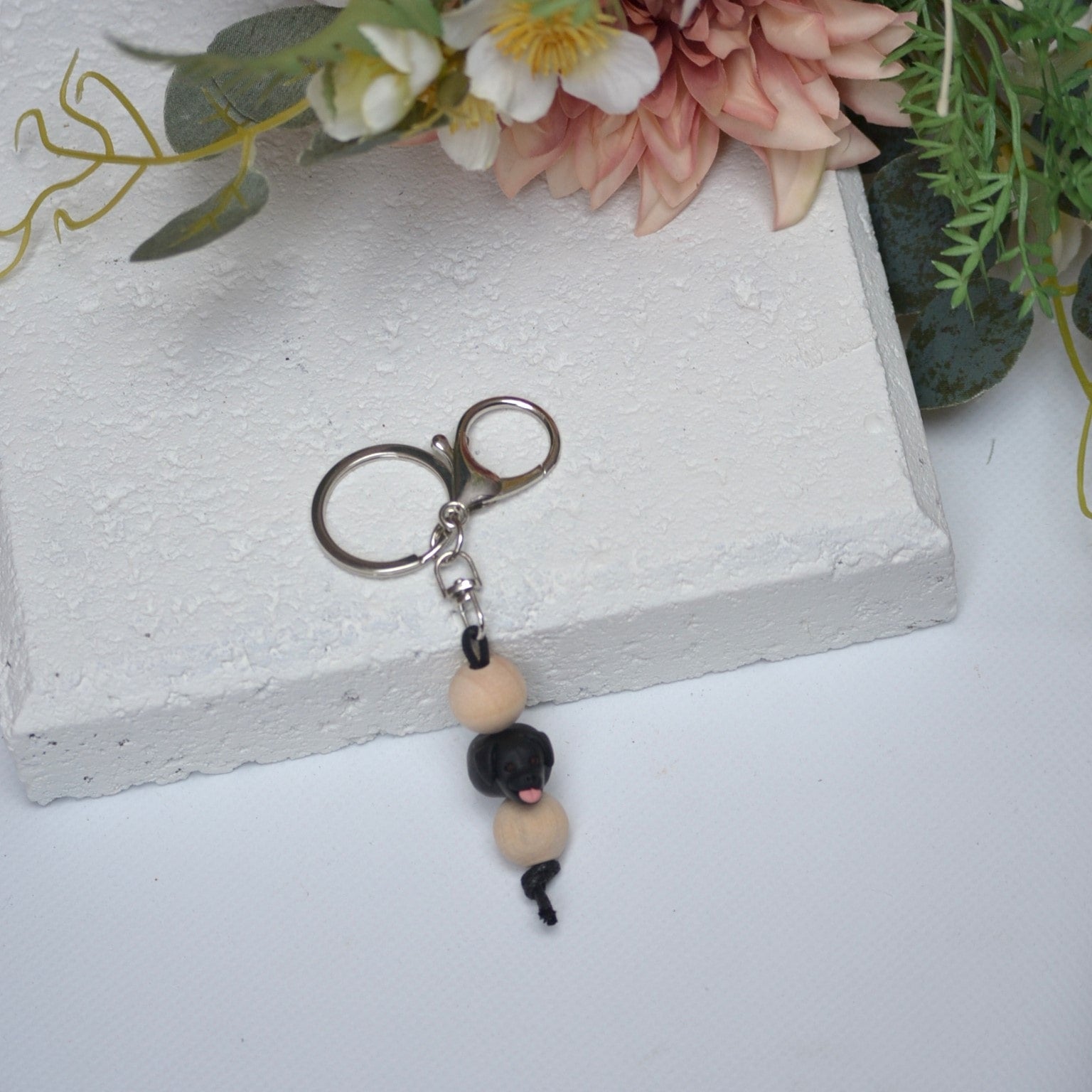 Handmade black labrador dog polymer clay and timber keying on white textured background with a pink flower in the background