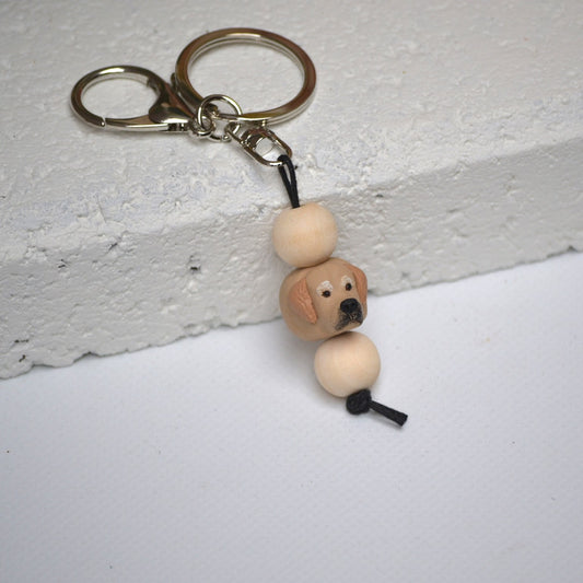 Handmade golden retriever dog polymer clay and timber keying on white textured background with a pink flower in the background