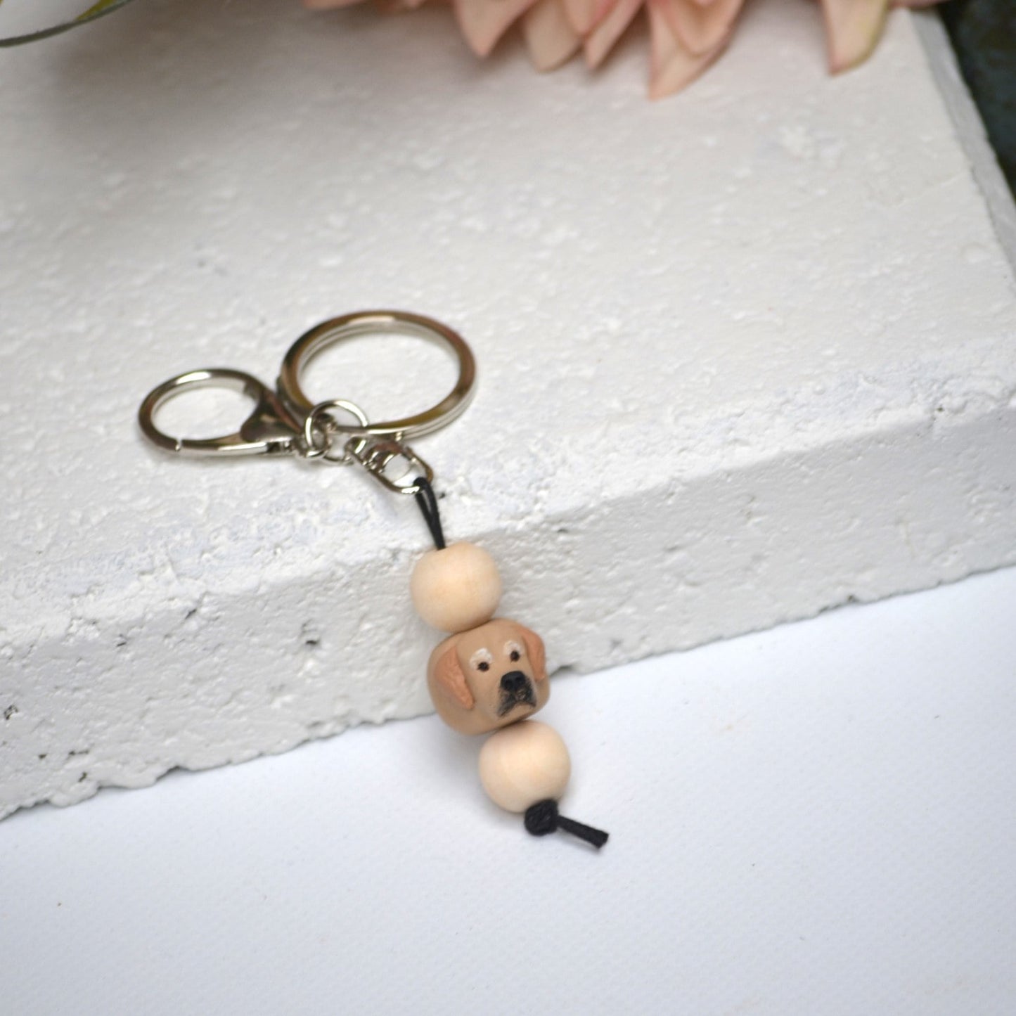 Handmade golden retriever dog polymer clay and timber keying on white textured background with a pink flower in the background
