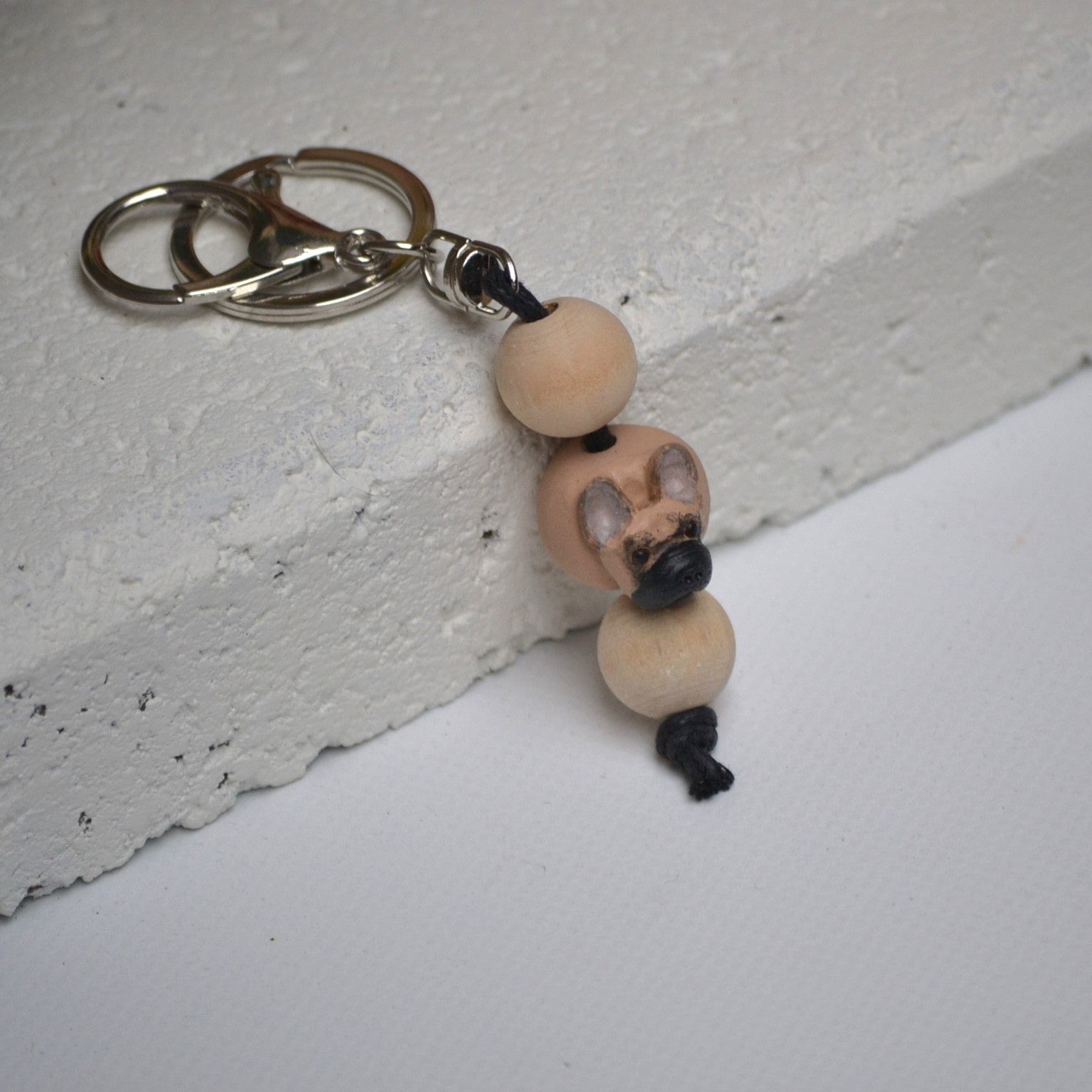 Handmade French Bulldog polymer clay and timber keying on white textured background with a pink flower in the background