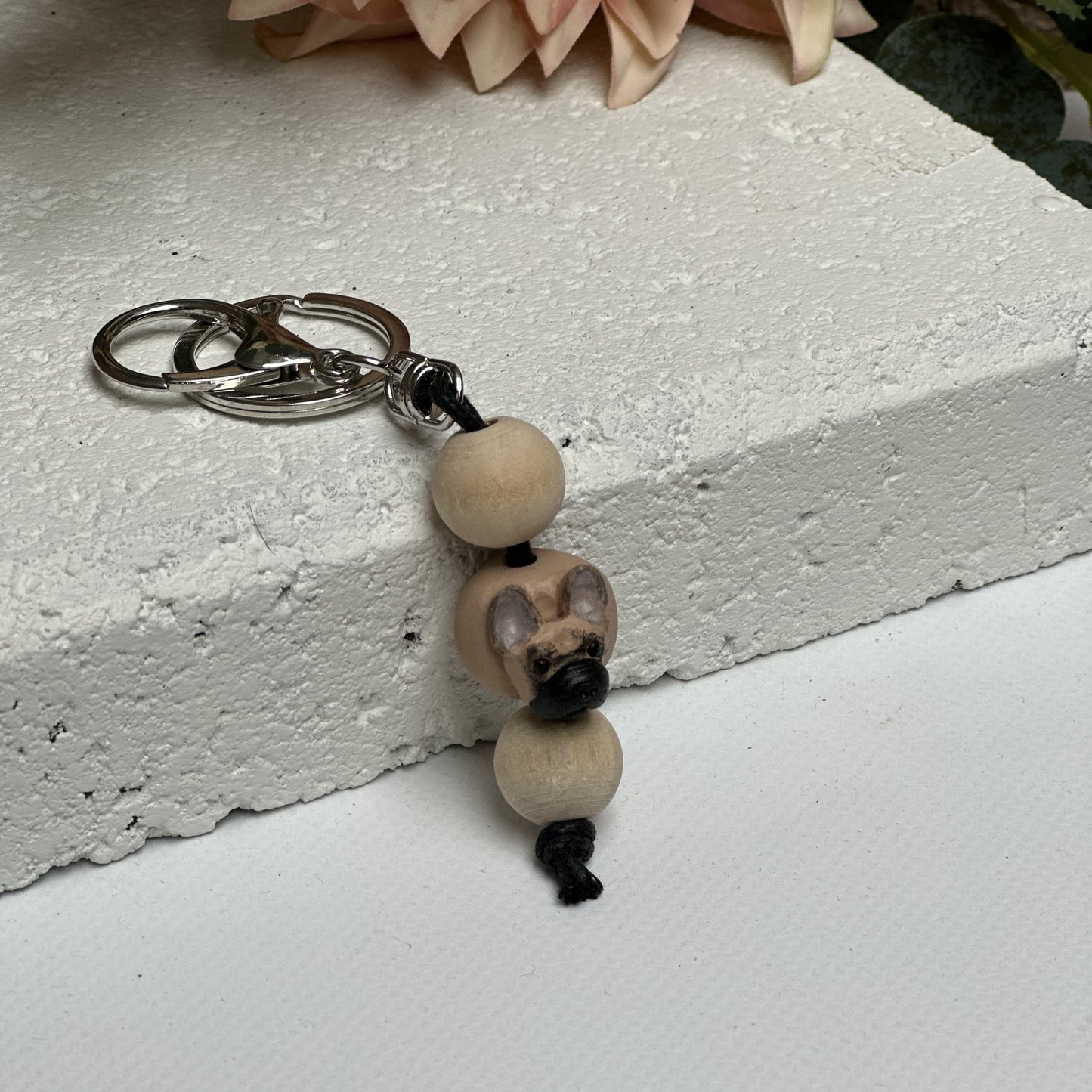 Handmade French Bulldog polymer clay and timber keying on white textured background with a pink flower in the background
