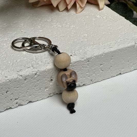 Handmade French Bulldog polymer clay and timber keying on white textured background with a pink flower in the background