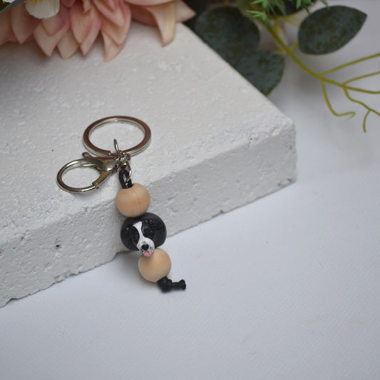 Handmade border collie dog polymer clay and timber keying on white textured background with a pink flower in the background