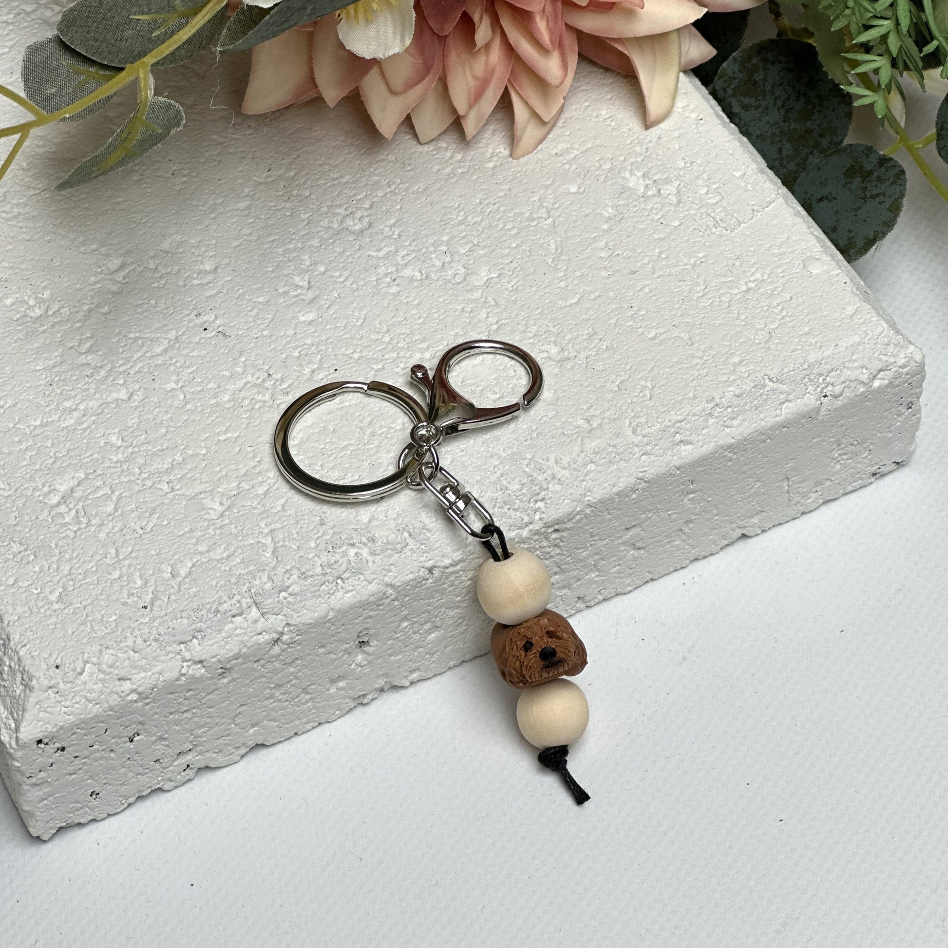 Handmade cavoodle dog polymer clay and timber keying on white textured background with a pink flower in the background