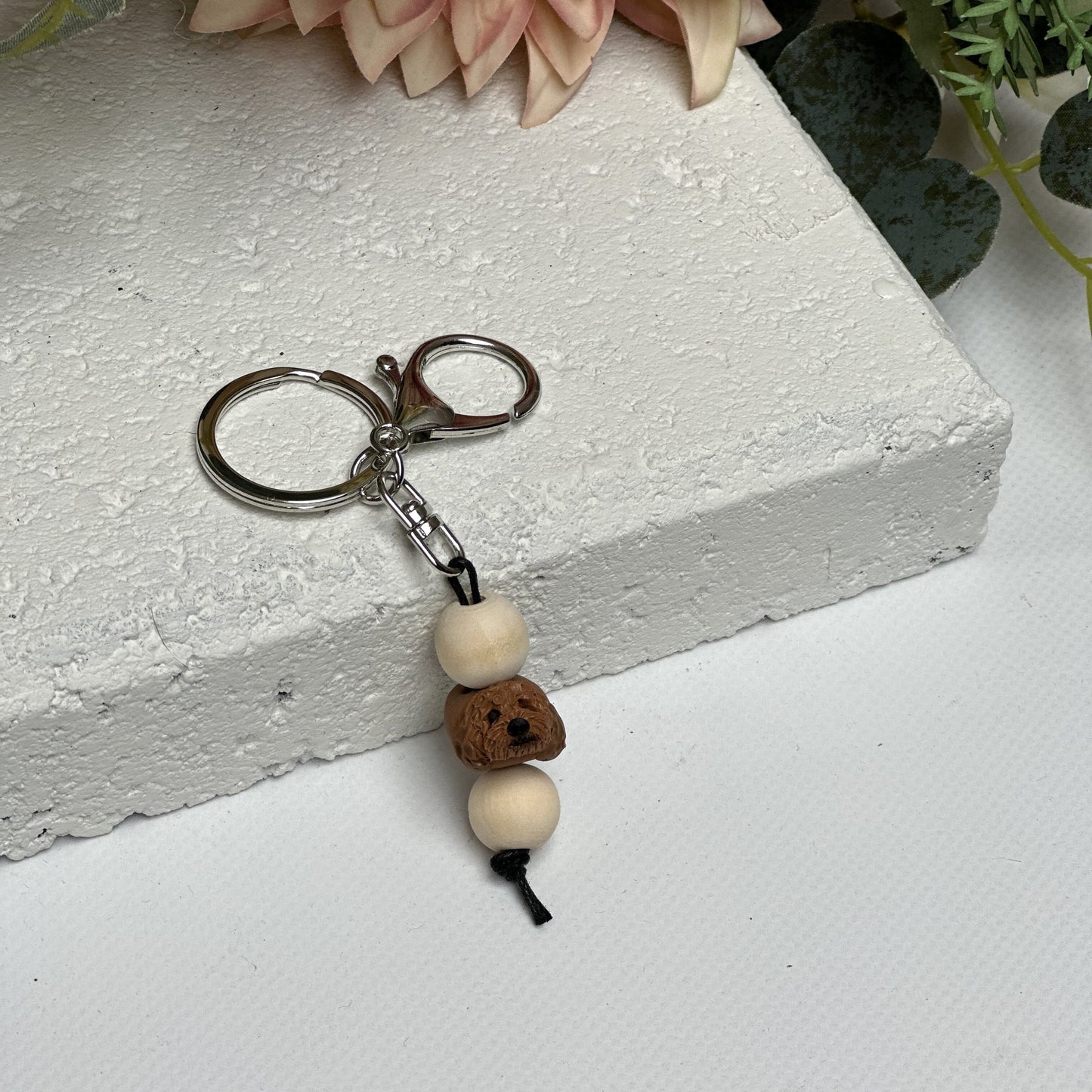 Handmade cavoodle dog polymer clay and timber keying on white textured background with a pink flower in the background