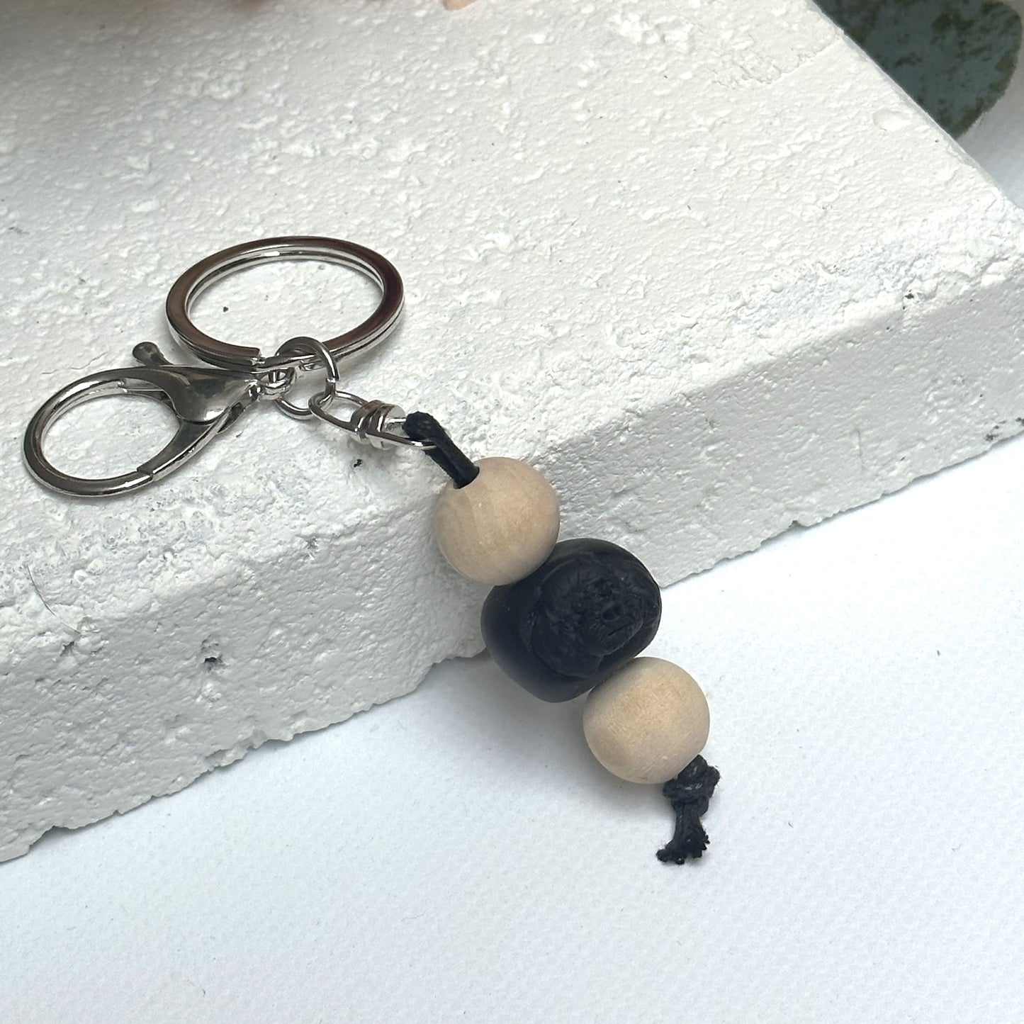 Handmade black poodle dog polymer clay and timber keying on white textured background with a pink flower in the background