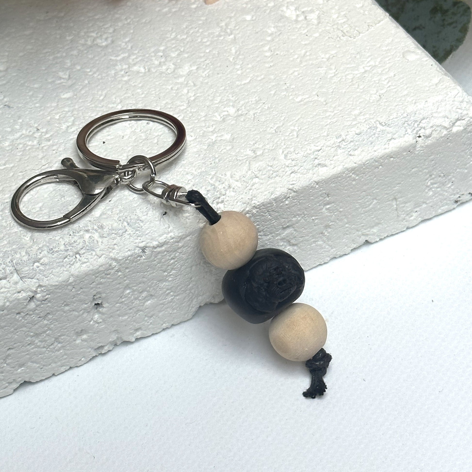 Handmade black poodle dog polymer clay and timber keying on white textured background with a pink flower in the background