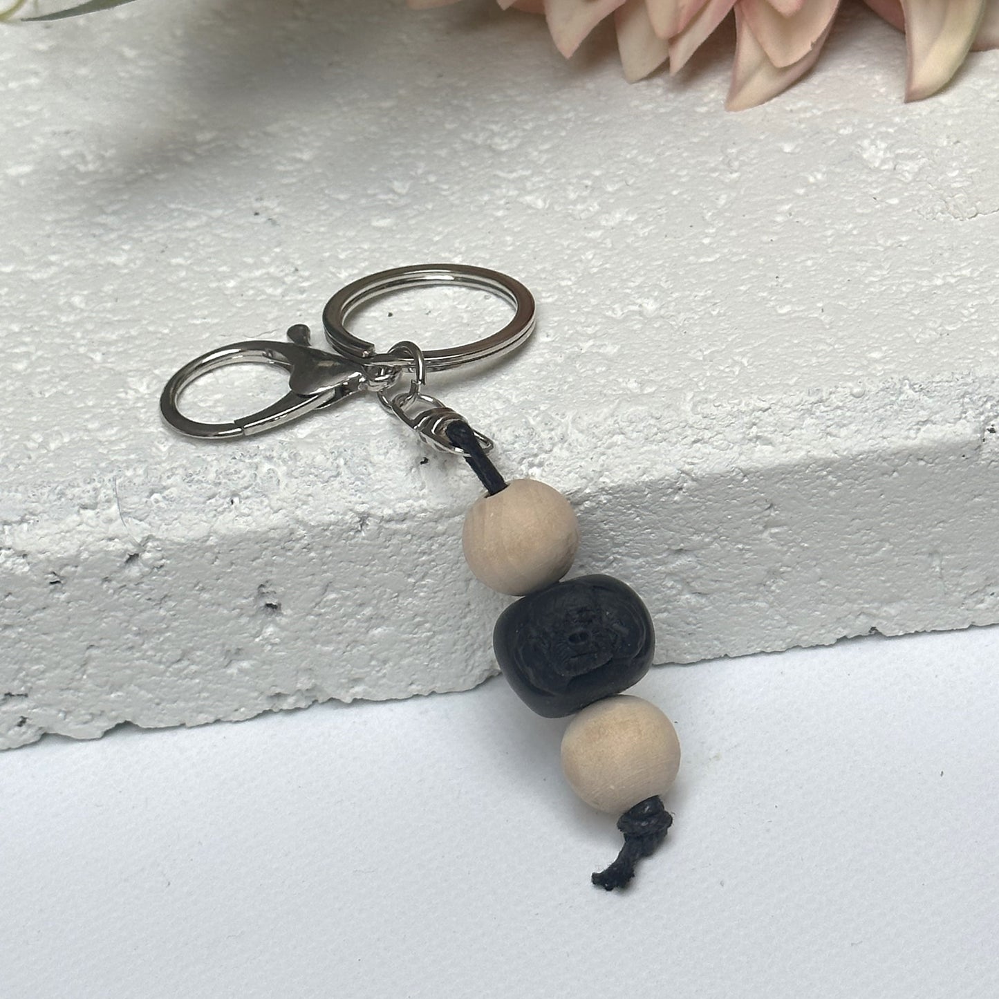 Handmade black poodle dog polymer clay and timber keying on white textured background with a pink flower in the background