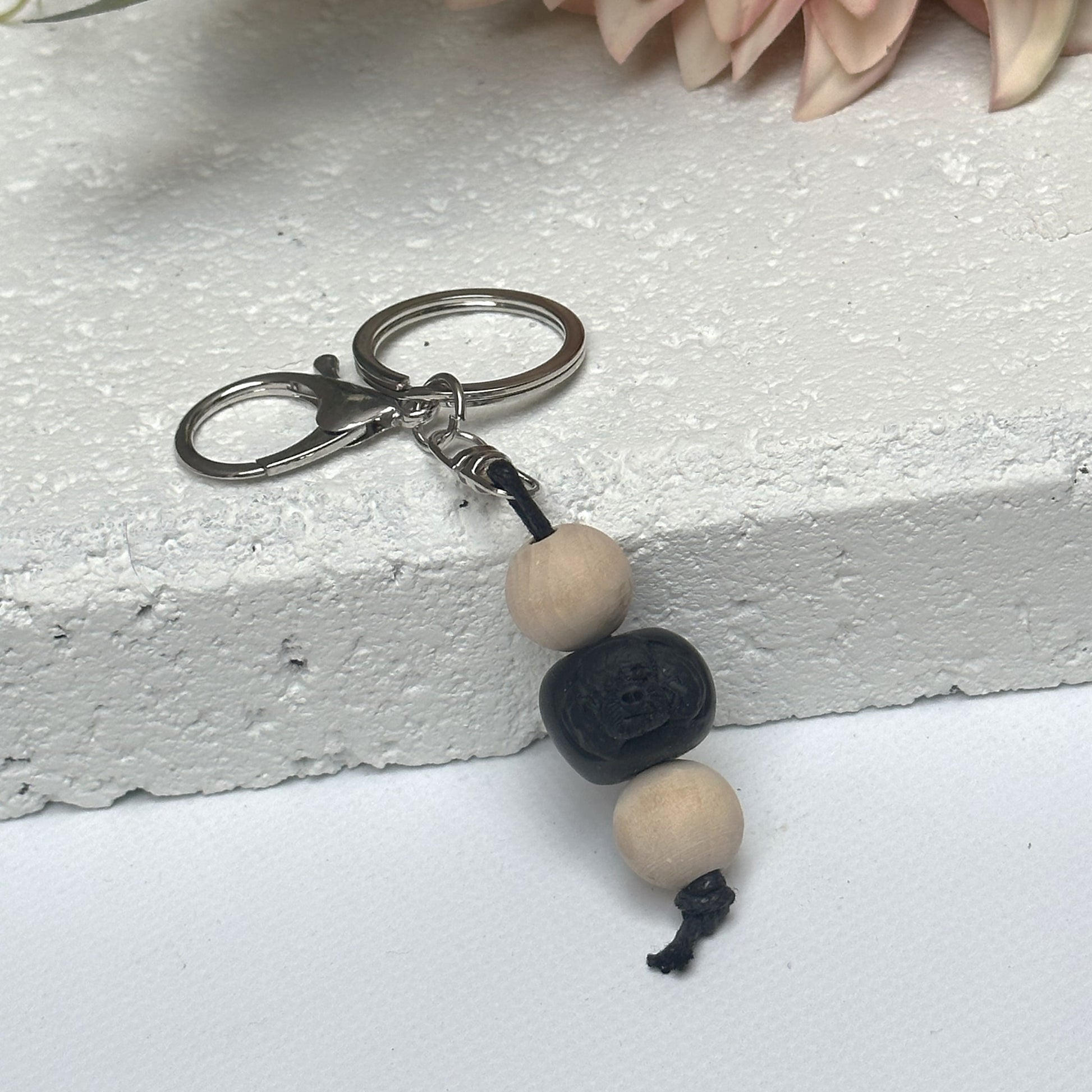 Handmade black poodle dog polymer clay and timber keying on white textured background with a pink flower in the background