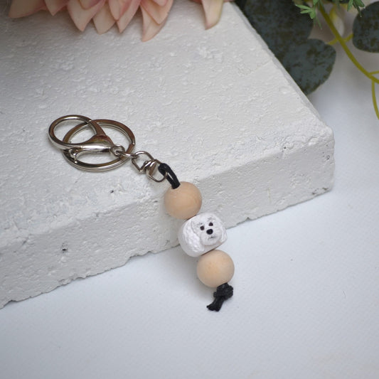 Handmade White Poodle dog polymer clay and timber keying on white textured background with a pink flower in the background