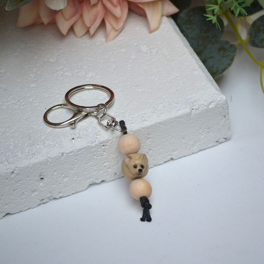 Handmade chihuahua dog polymer clay and timber keying on white textured background with a pink flower in the background