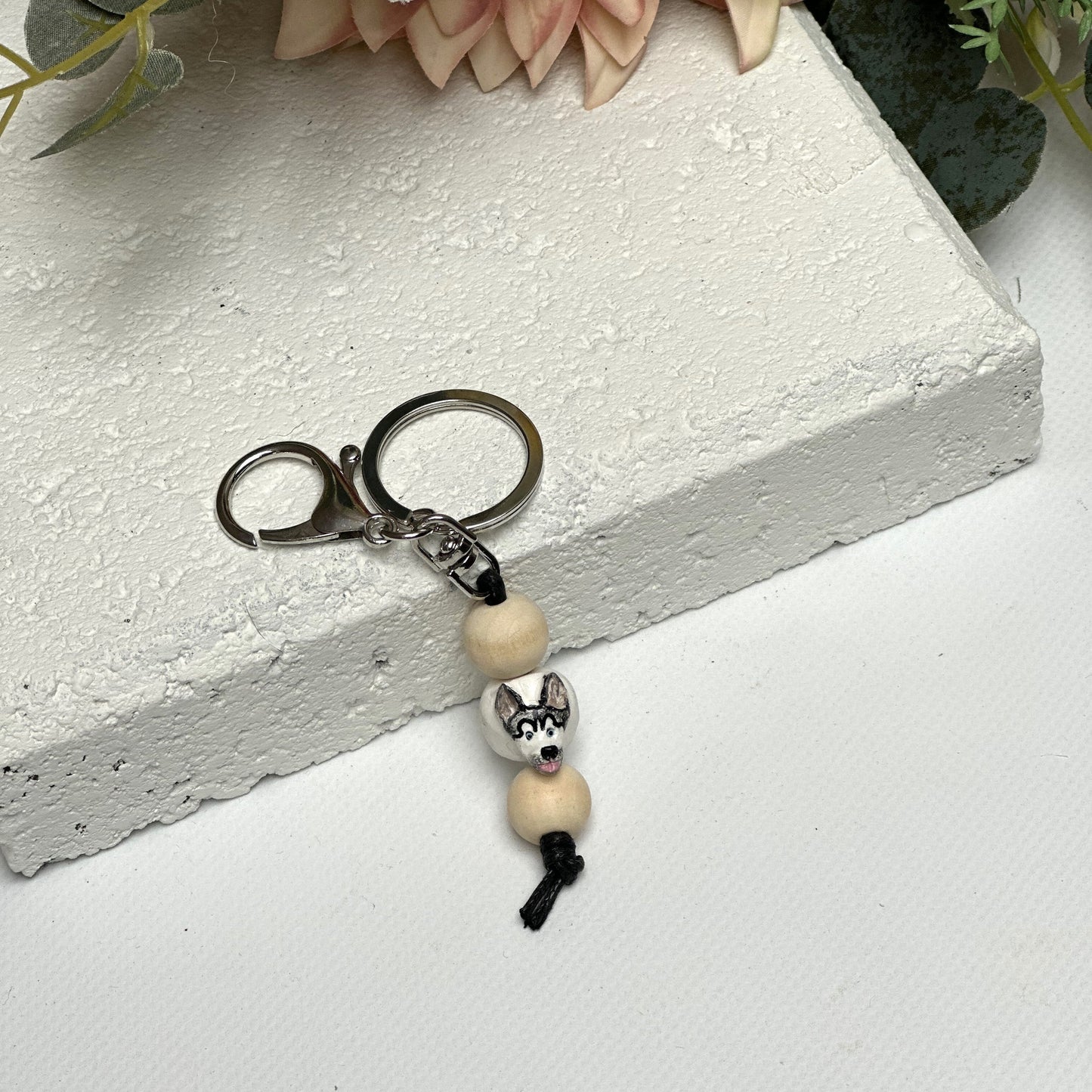 Handmade husky dog polymer clay and timber keying on white textured background with a pink flower in the background