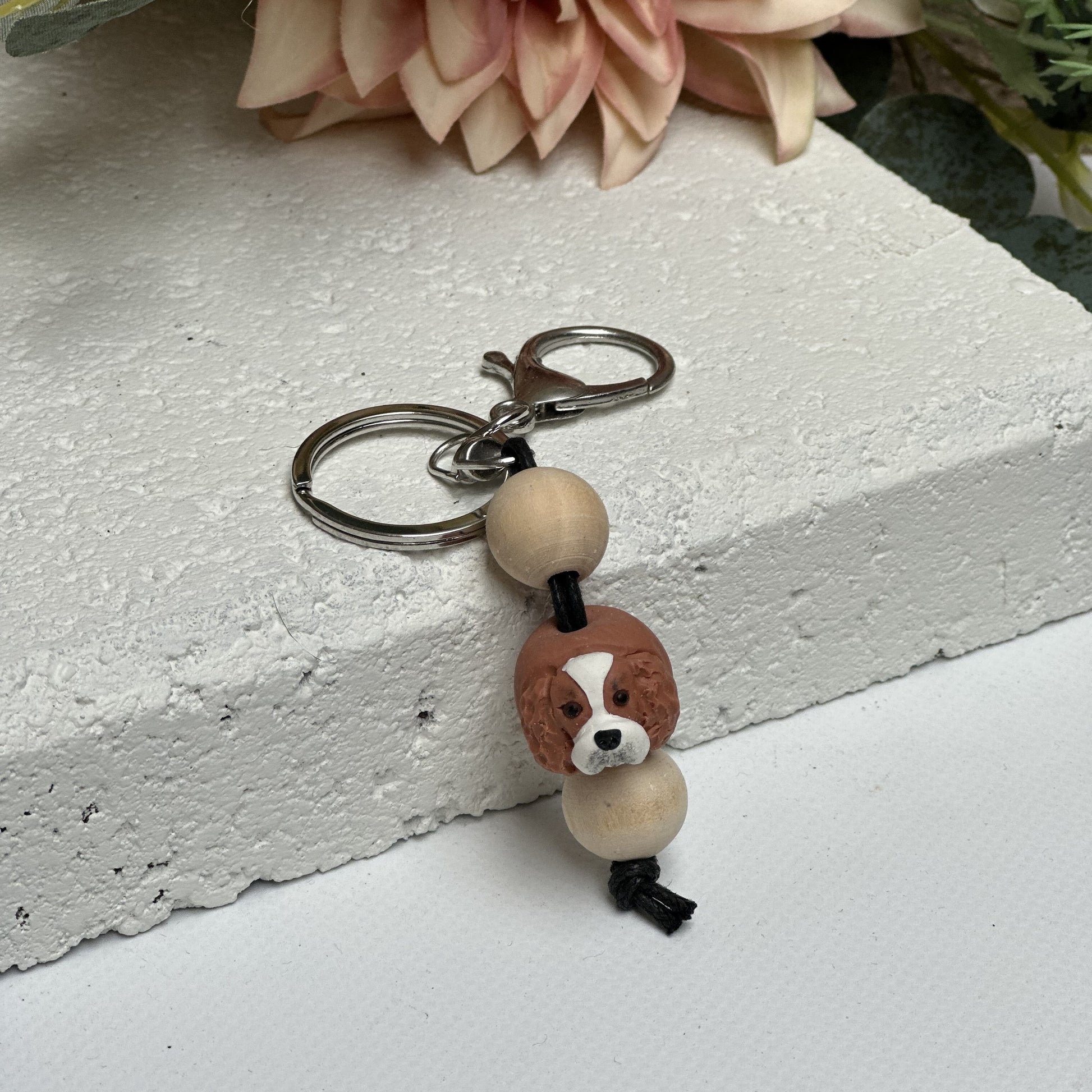 Handmade cavalier king charles spaniel polymer clay and timber keying on white textured background with a pink flower in the background
