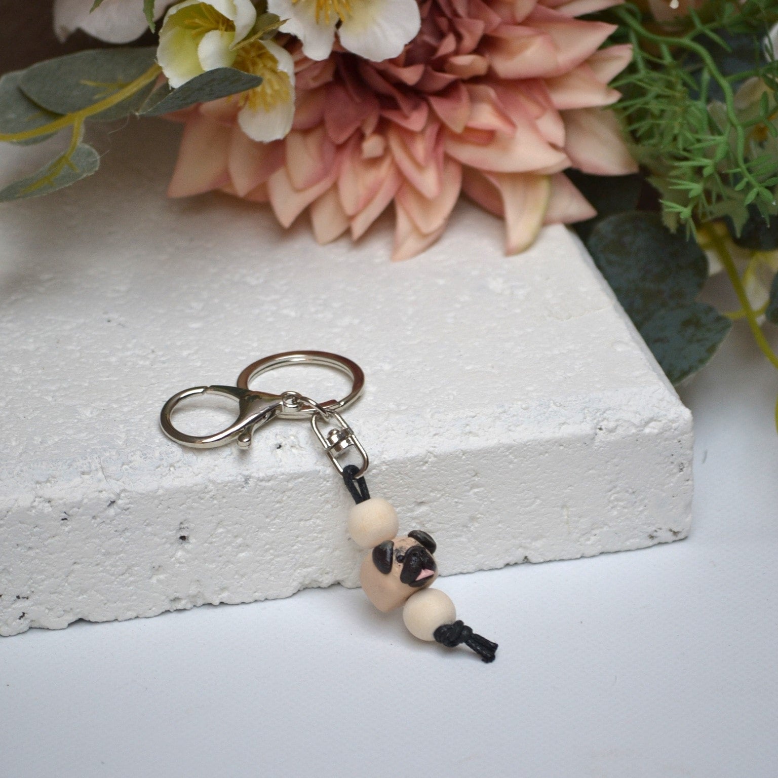 Handmade pug polymer clay and timber keying on white textured background with a pink flower in the background