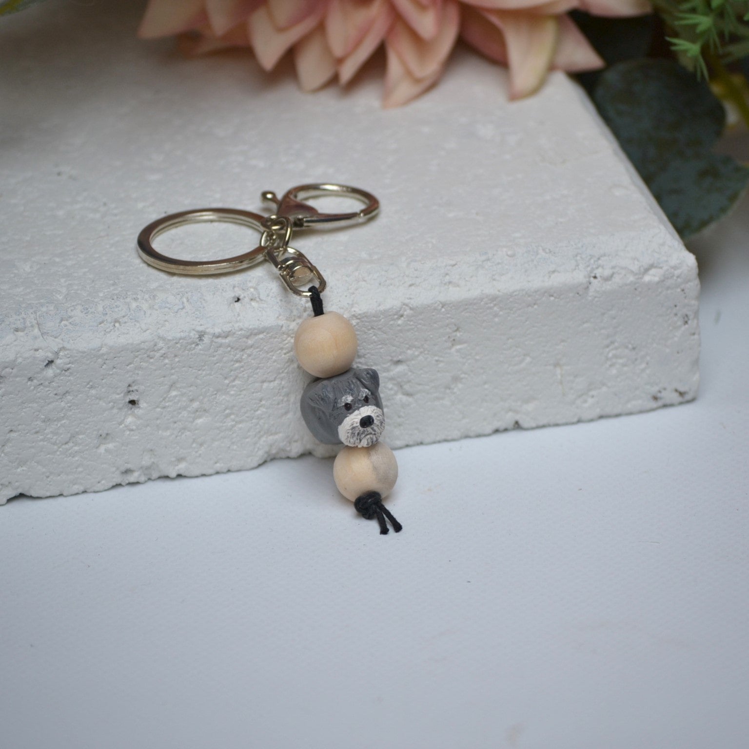 Handmade Schnauzer dog polymer clay and timber keying on white textured background with a pink flower in the background