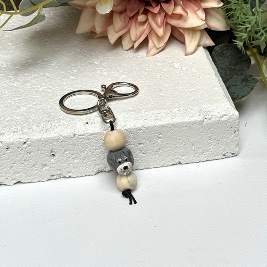 Handmade Schnauzer dog polymer clay and timber keying on white textured background with a pink flower in the background