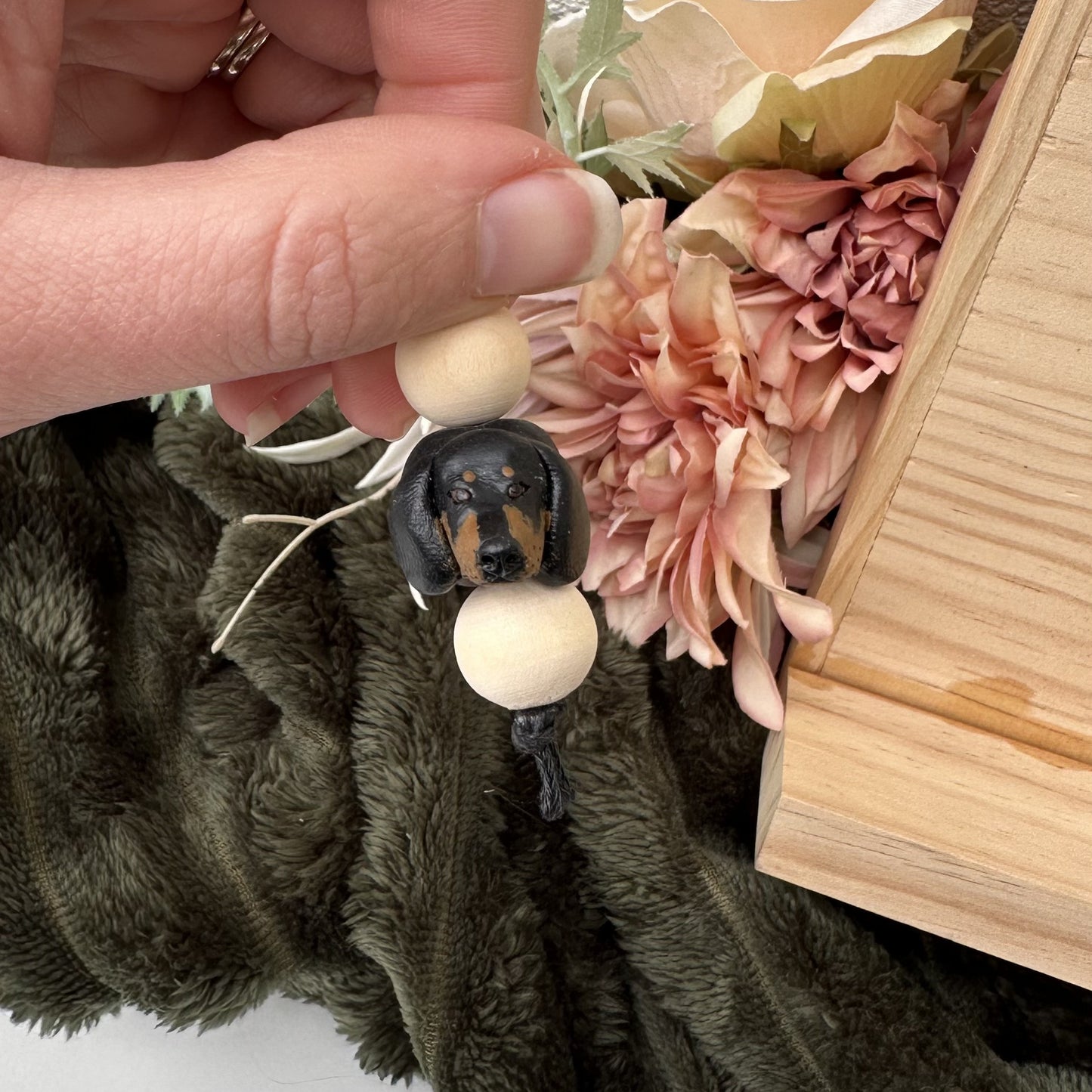 Small dog figurine with a wooden base held by a hand, surrounded by flowers and fabric.
