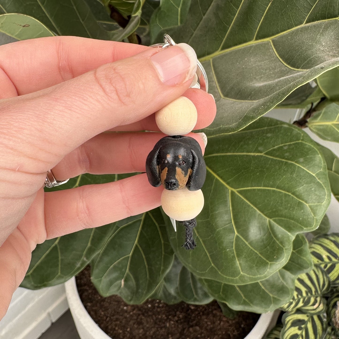 Hand holding a keychain with a dachshund dog design against a leafy green background