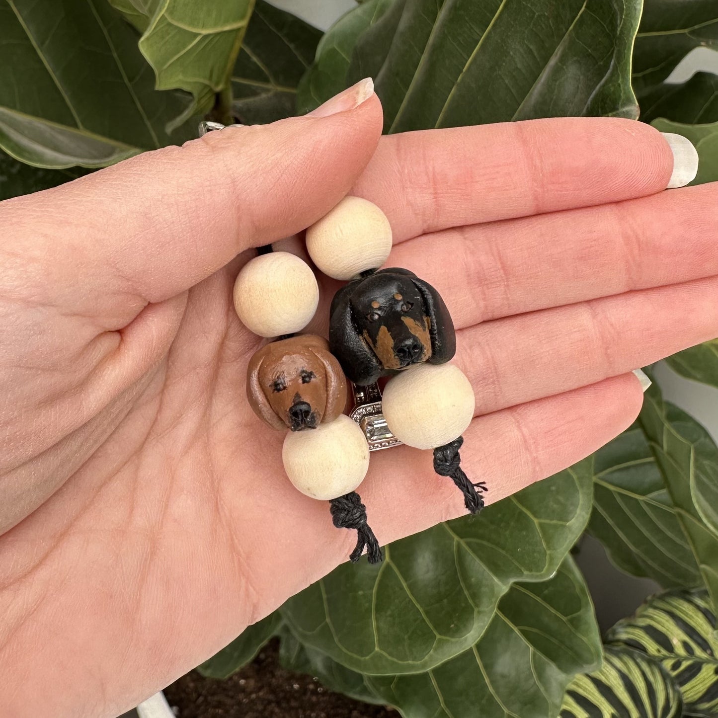 Hand holding two dachshund dog-shaped beads on a string with a green leafy background