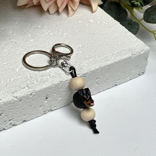 Handmade Kelpie dog polymer clay and timber keying on white textured background with a pink flower in the background