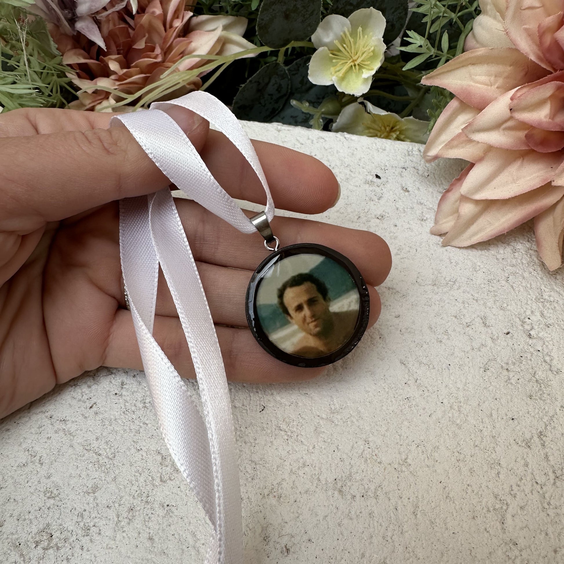 Memorial photo charm of father for bridal bouquet, pictured in front of florals.