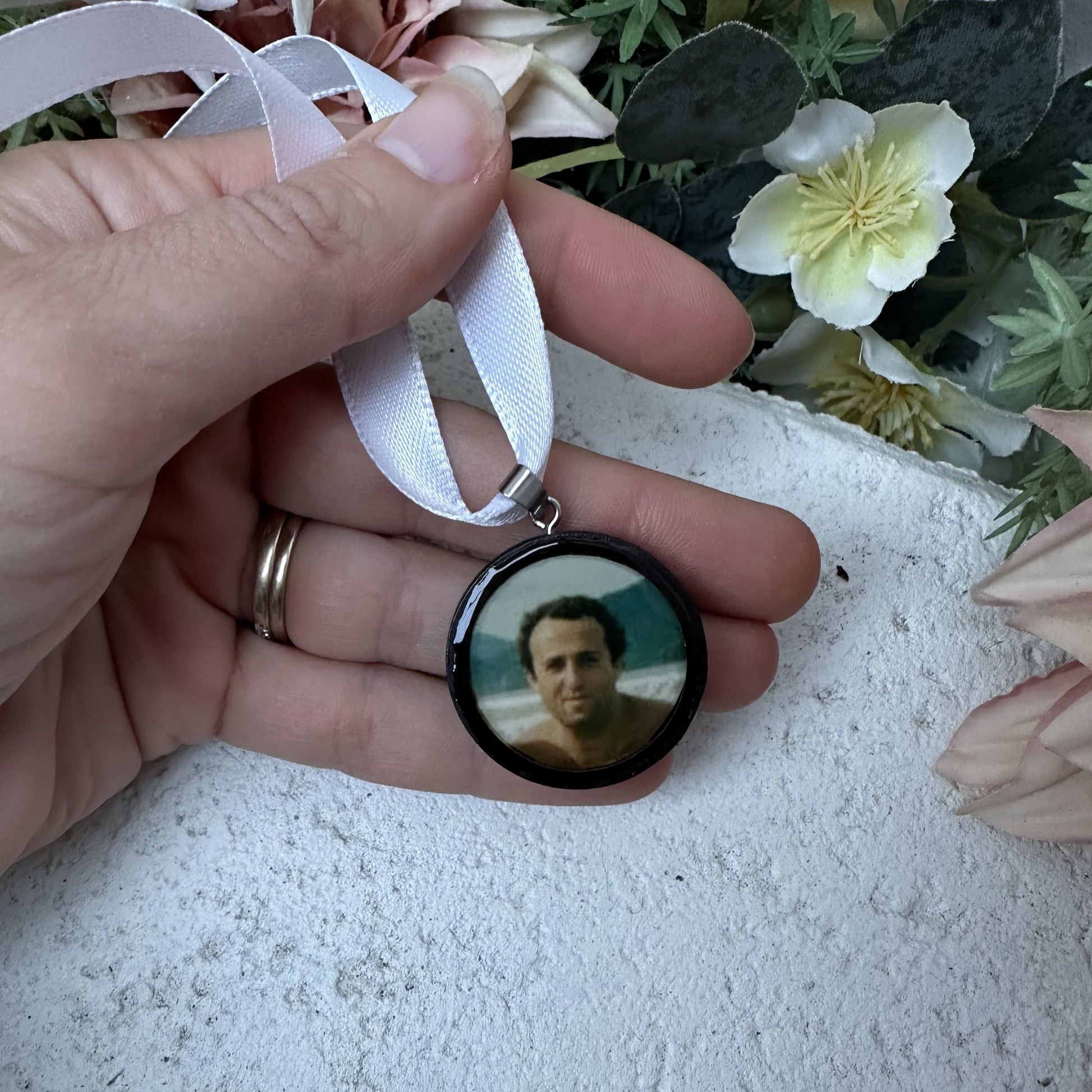 Memorial photo charm of father for bridal bouquet, pictured in front of florals.