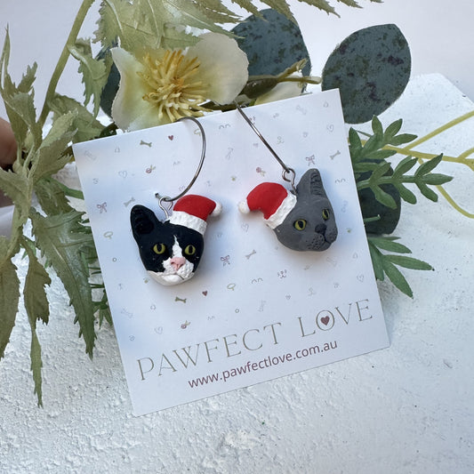 Handmade mismatched custom cat hoop earrings wearing santa hats.