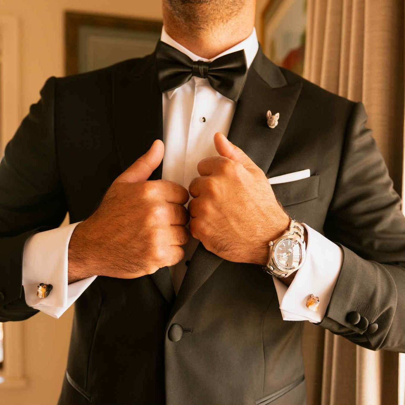 Man adjusting his black tuxedo jacket indoors, also wearing a custom pet lapel pin and dog cufflinks made by Pawfect Love.