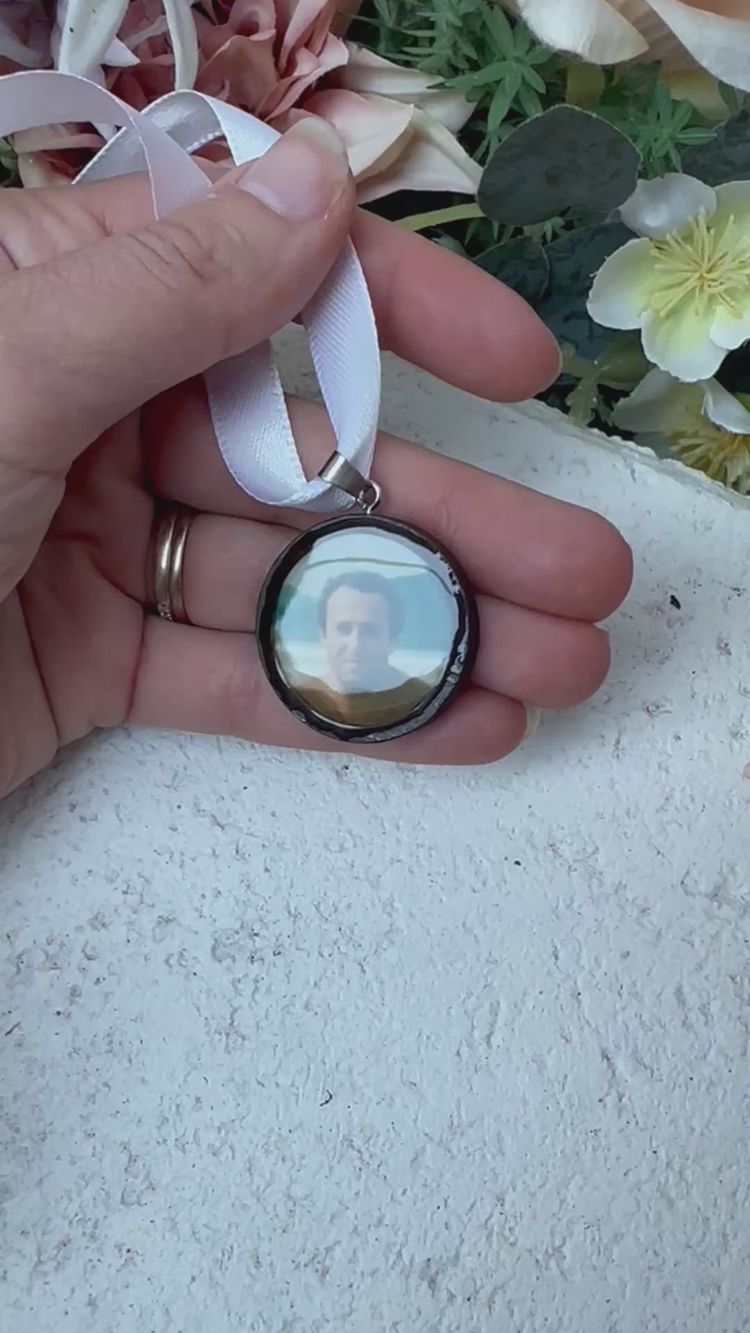 Video of timber memorial photo charm of father for bridal bouquet, pictured in front of florals. Surface gloss from resin is evident.