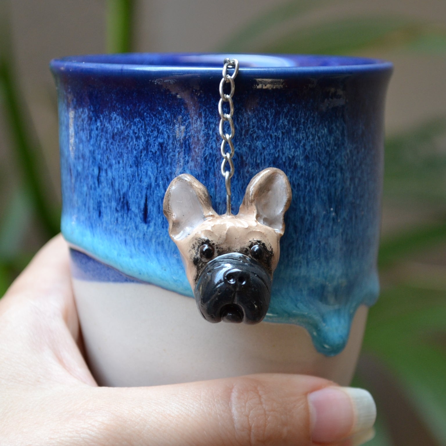 Handmade custom pet face mesh ball tea strainer being used in a blue ceramic cup..