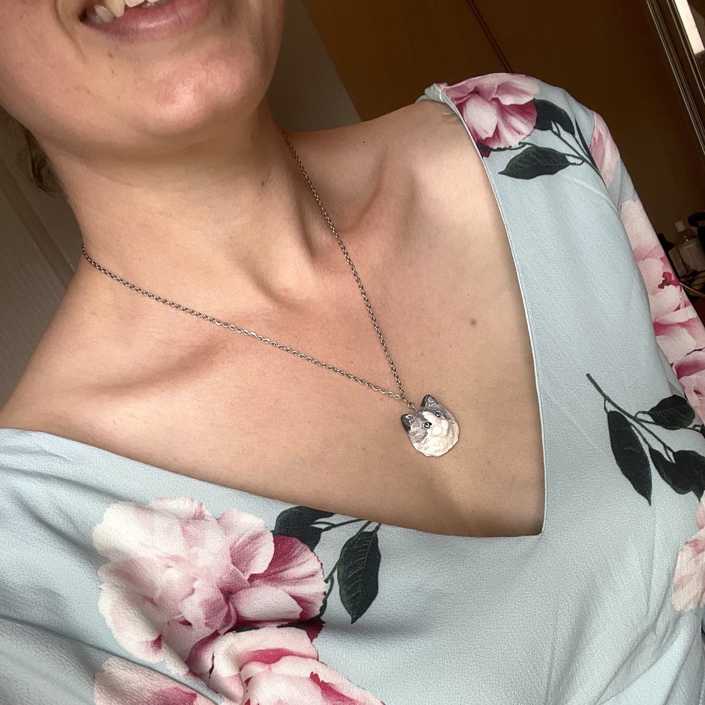 Handmade custom cat necklace pendant on chain, worn around the neck of a woman in a blue floral dress..