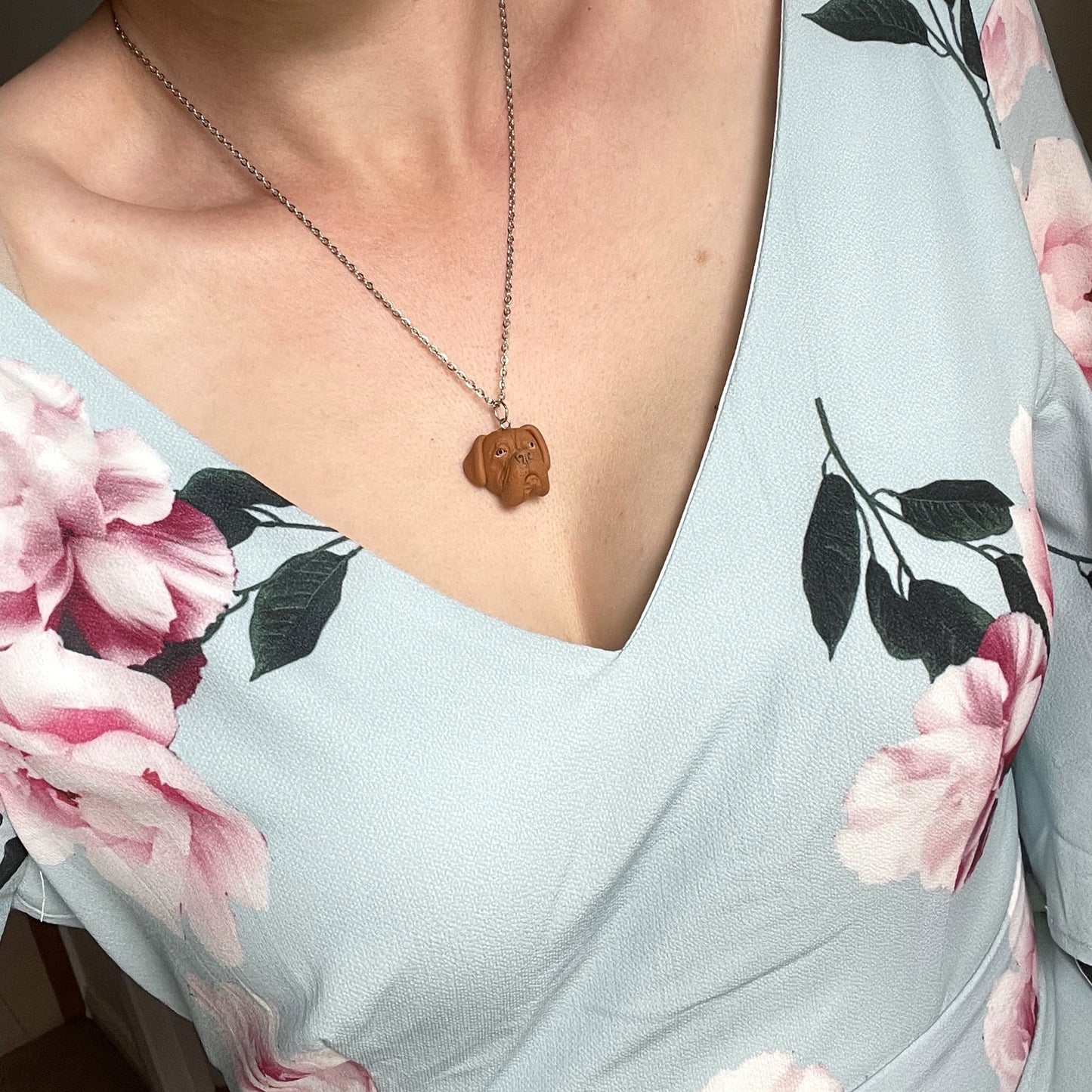 Handmade custom dogue de bordeaux face pendant on silver chain worn around the neck of a woman wearing a floral blue dress.