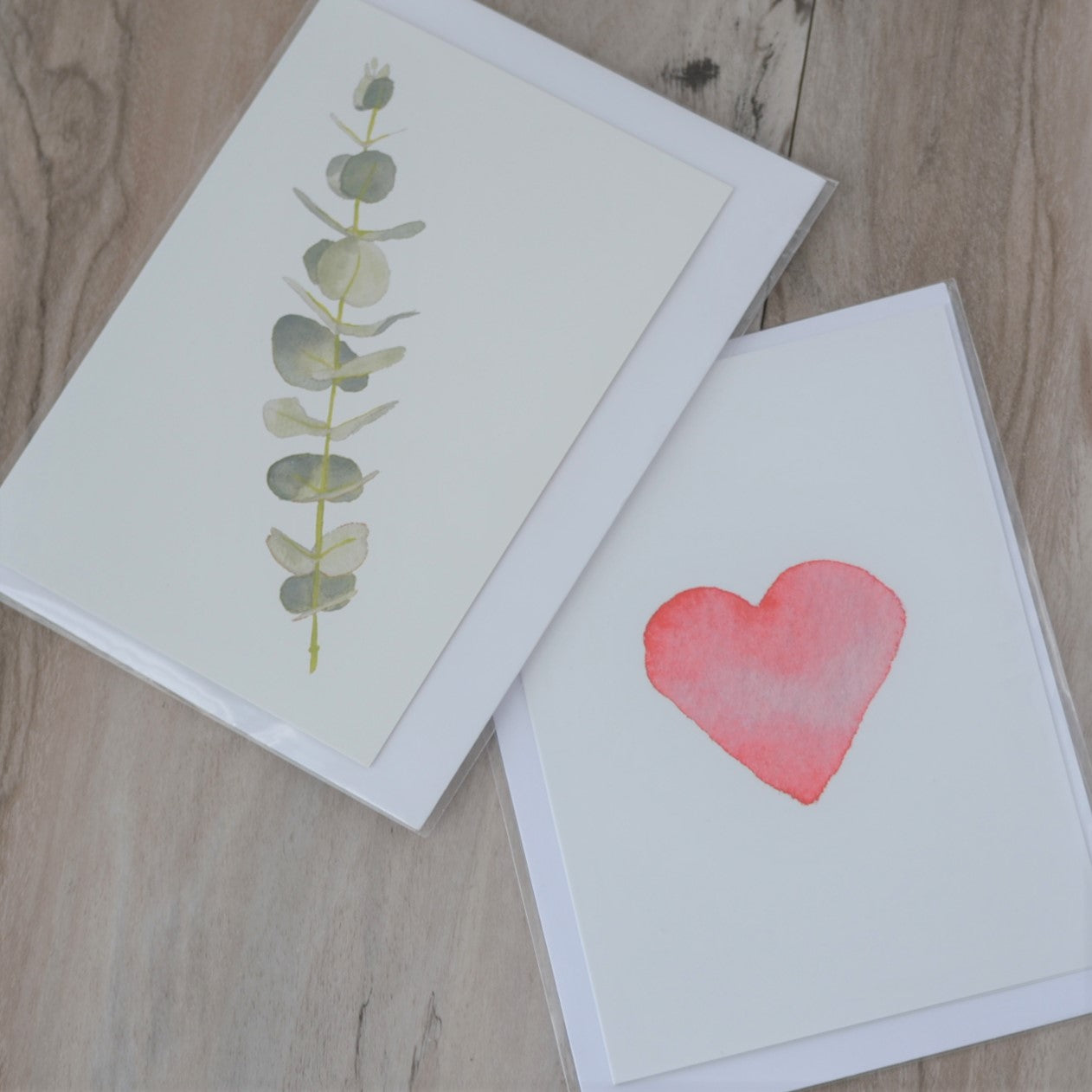 Two watercolour print greeting cards overlapping on a timber flooring background