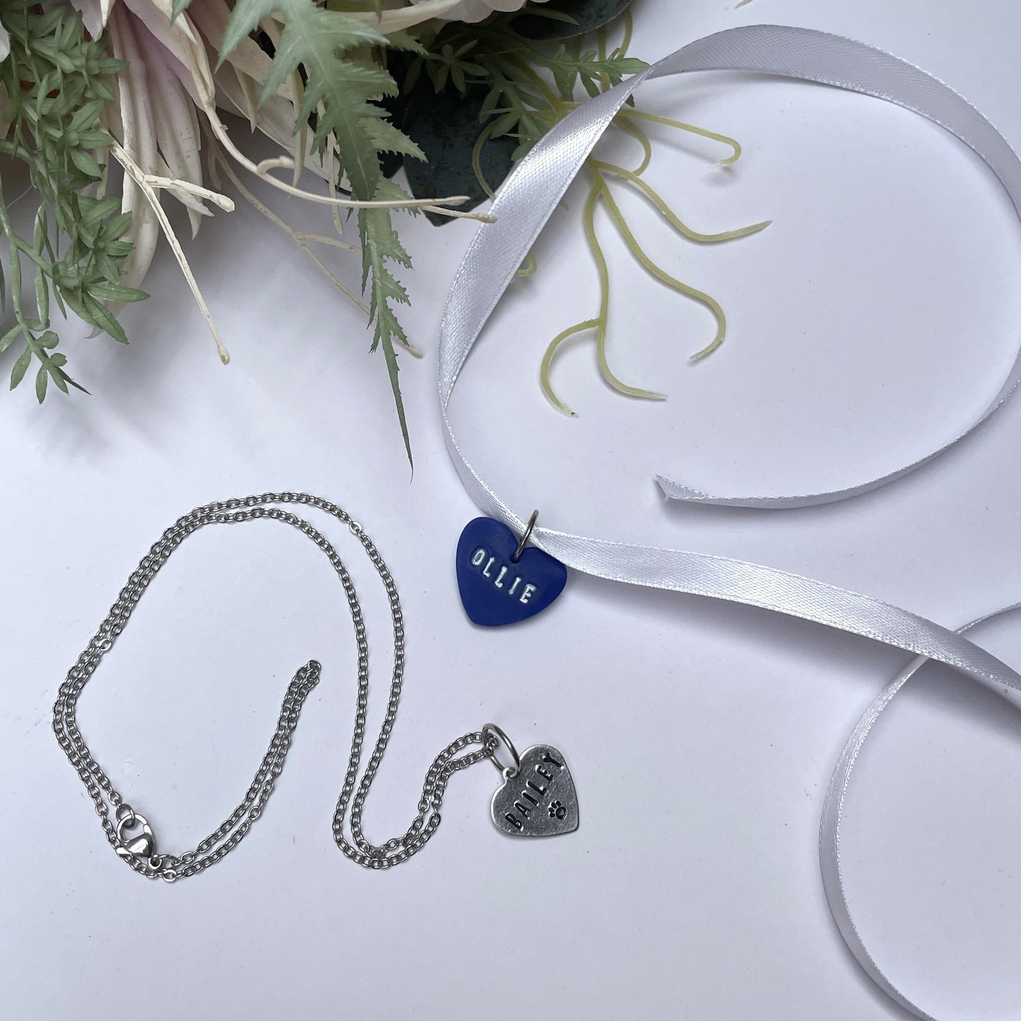 Two bouquet pendant charms with dog names on. One displayed on a ribbon, the second on a silver necklace chain.