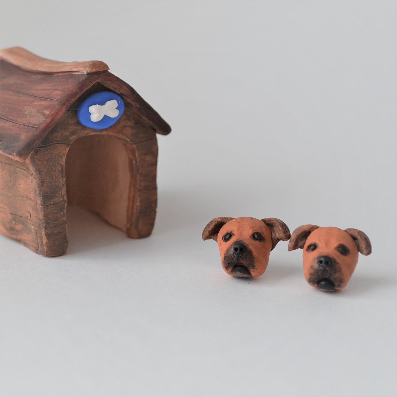 Handmade polymer clay Staffy stud earrings shown styled beside mini kennel